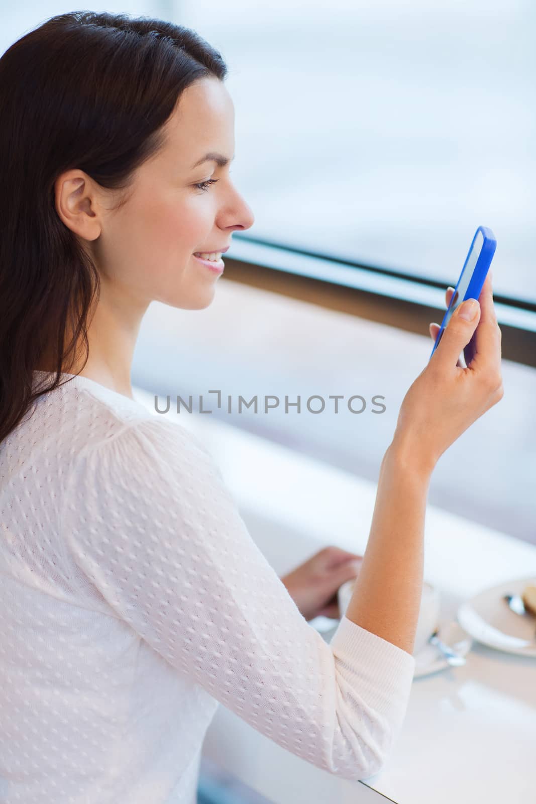 leisure, drinks, people, technology and lifestyle concept - smiling young woman with smartphone drinking coffee at cafe