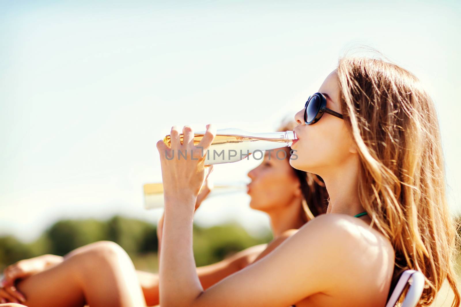 summer holidays and vacation - girls in bikinis with drinks on the beach chairs