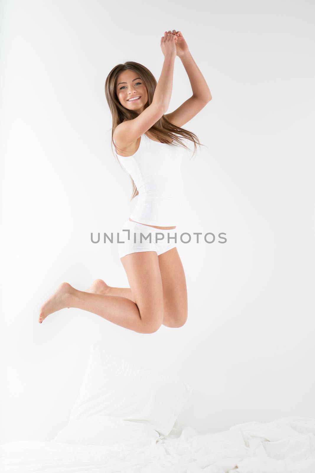 Cute young beautiful girl at morning jumping on the bed