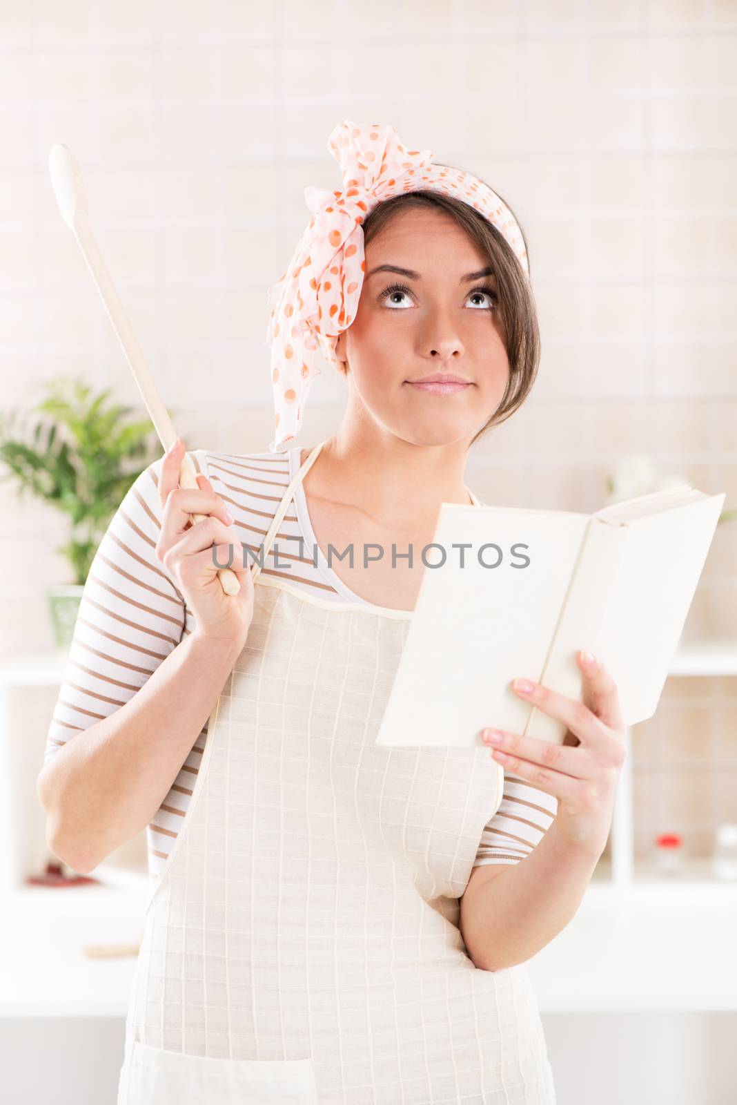 Happy woman reading cookbook and thinking in the kitchen