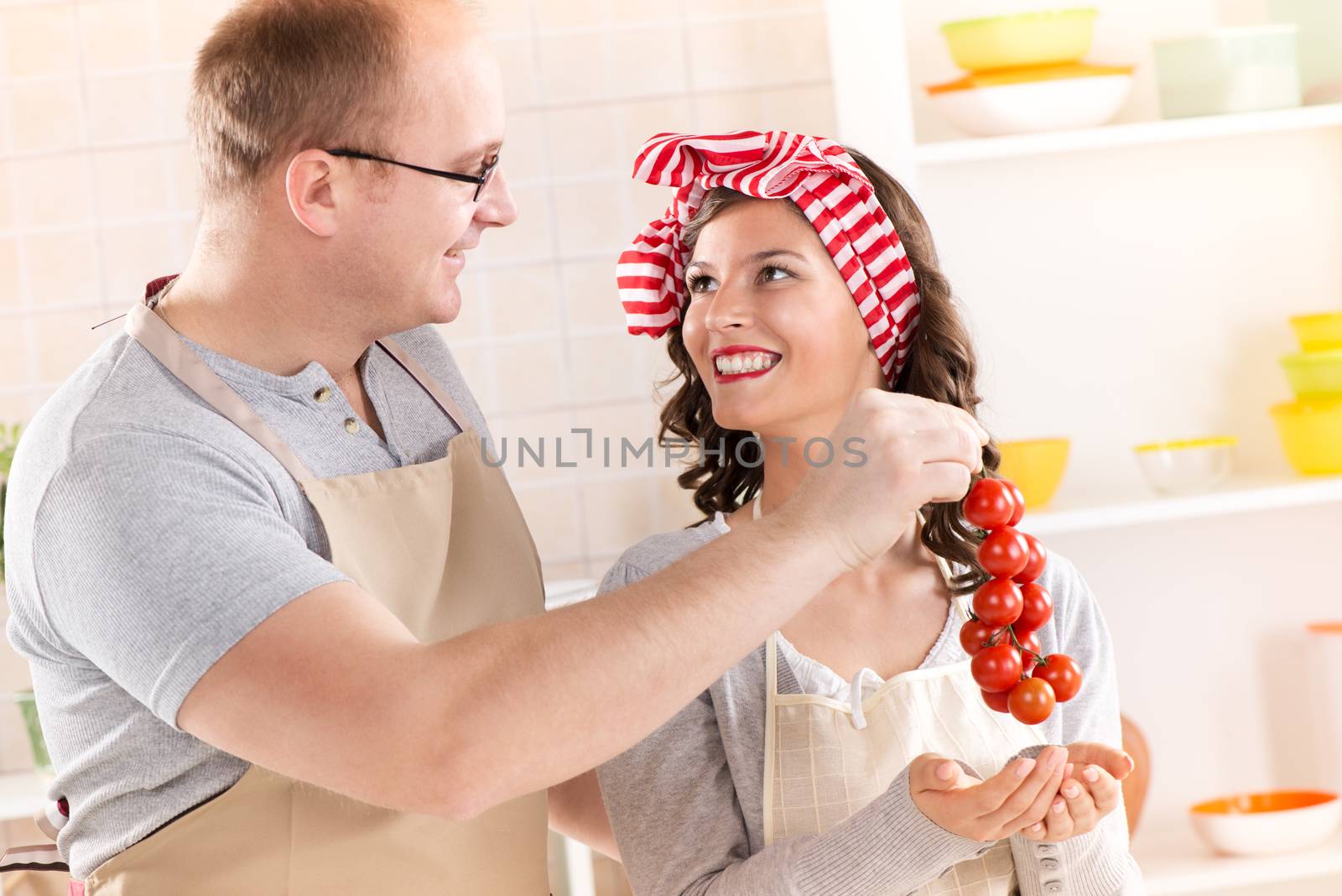 Happy couple holding cherry tomato in the kitchen. Close-up.