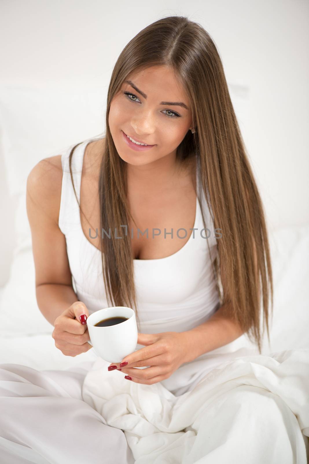 Cute young beautiful woman drinking coffee in the bed.