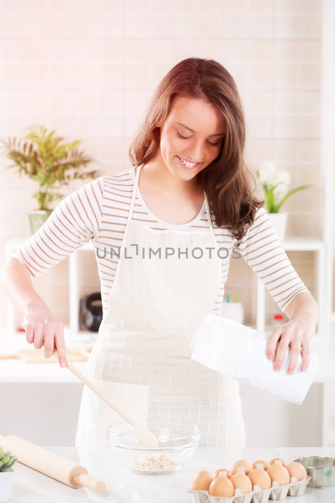 Happy young woman making dough in the kitchen.