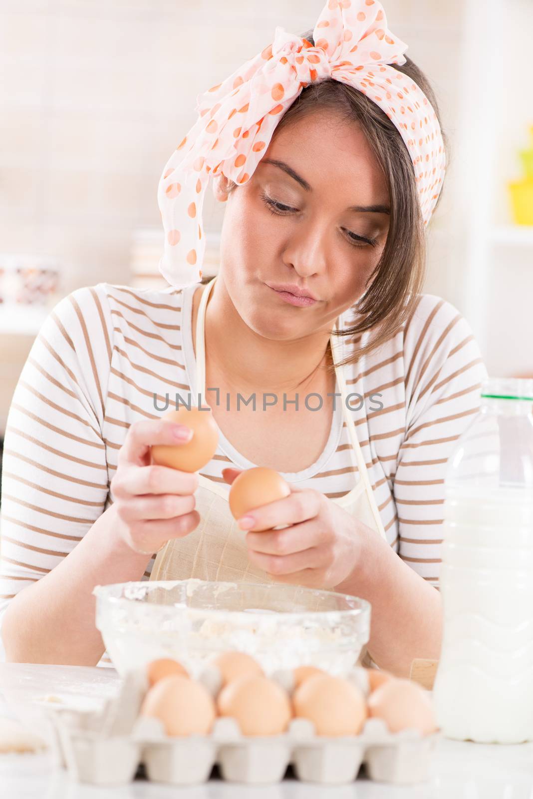 Beautiful young woman making dough in the kitchen. She is breaking eggs.