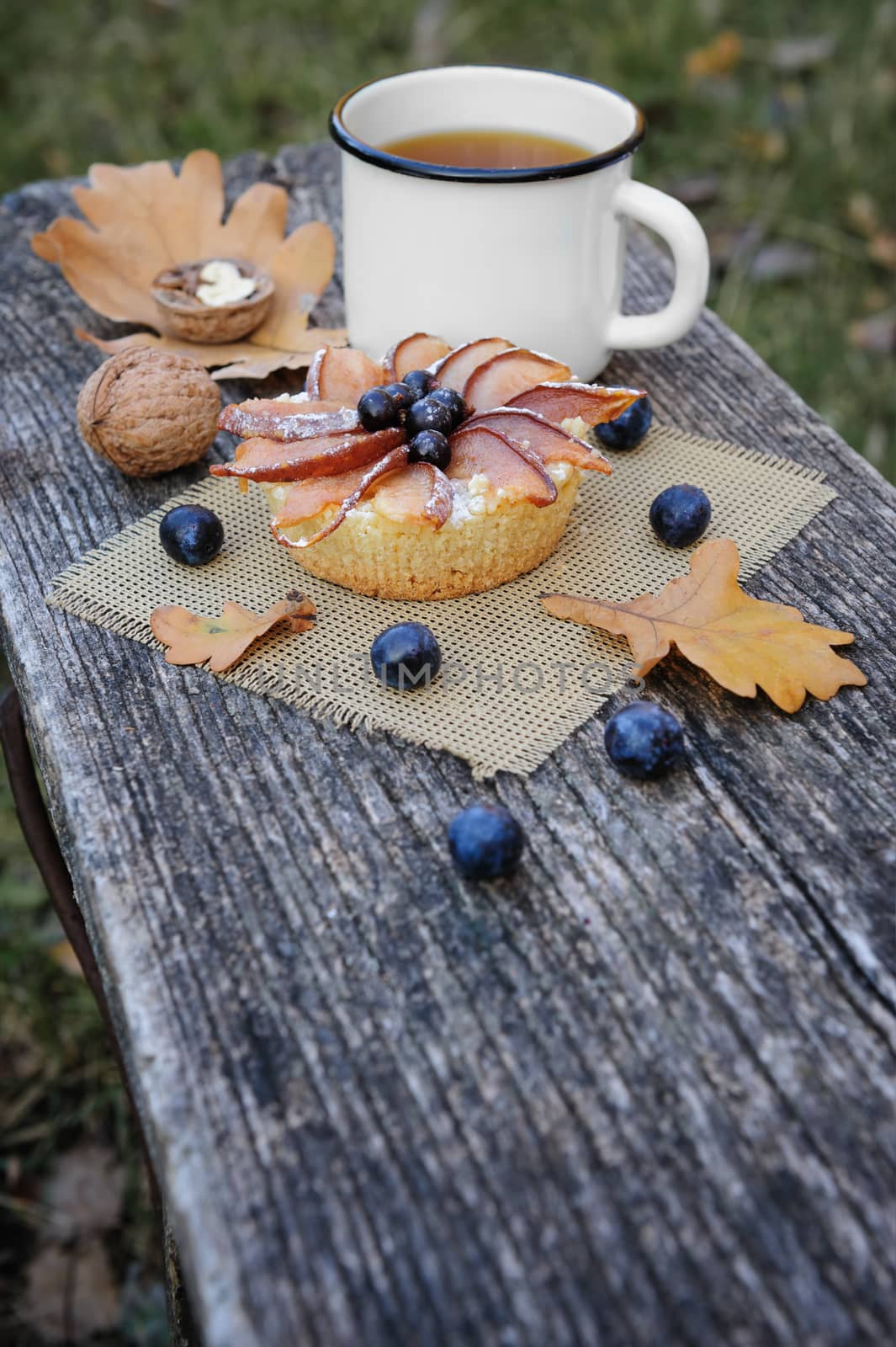 Romantic autumn still life with basket cake, cup of tea, walnuts, blackthorn berries and leaves, in cold colors