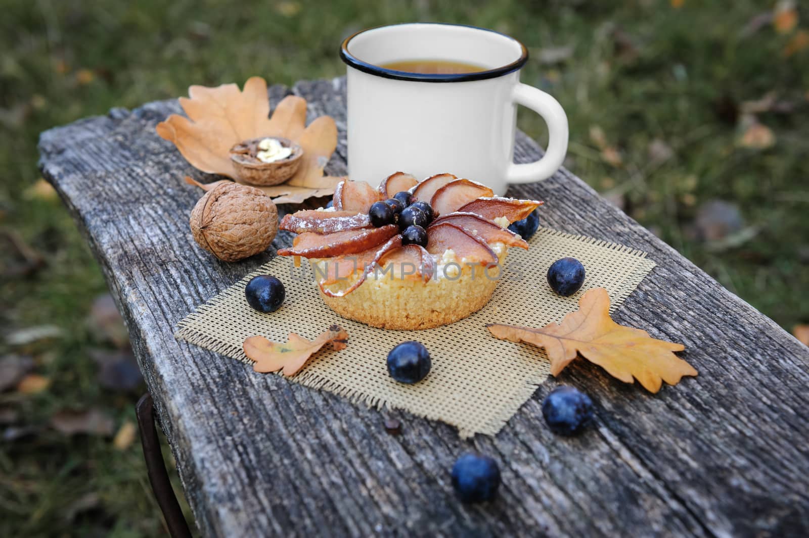 Romantic autumn still life with basket cake, cup of tea, walnuts, blackthorn berries and leaves, in cold colors
