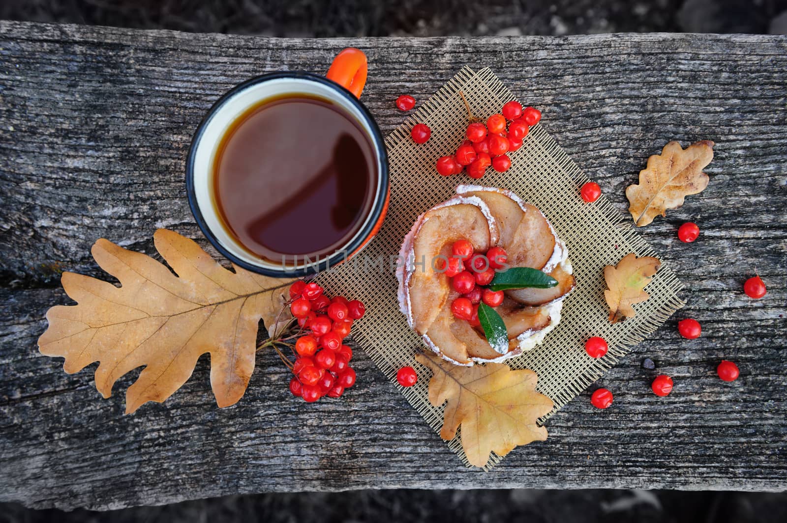 Romantic autumn still life with basket cake, cup of tea, rowan berries and leaves at wooden board, top view