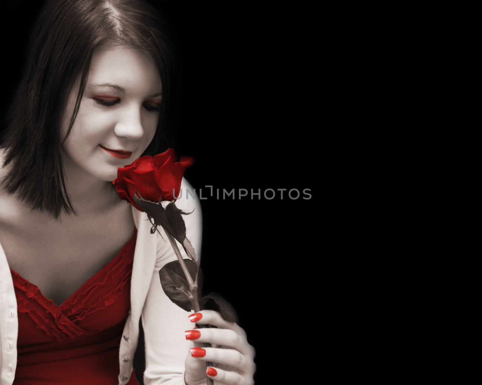 A beautiful woman dreams passionately as she glances at her red rose in this artisticly toned image.