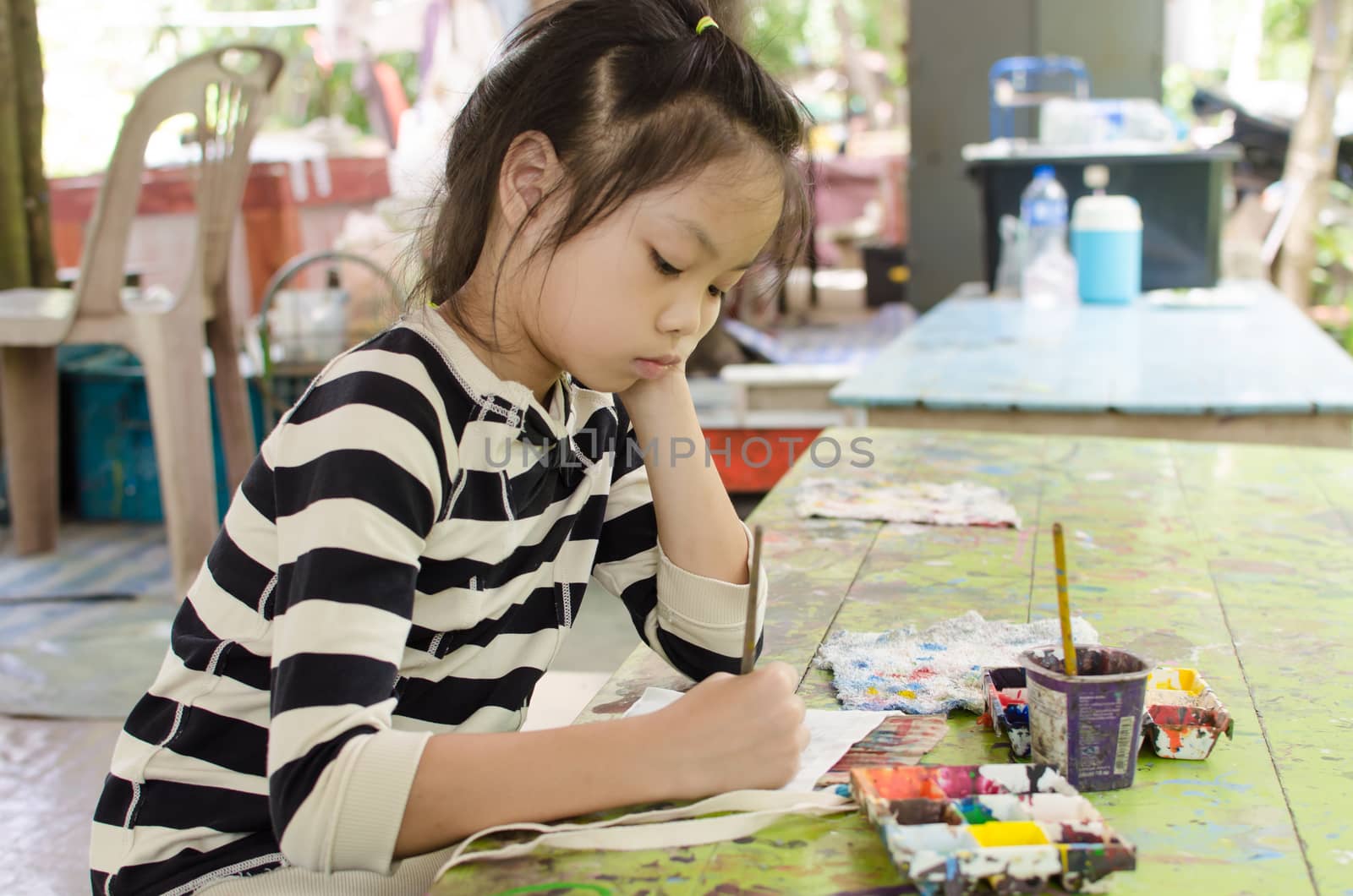 A young girl Asia sitting at the table and draws colored watercolor picture.