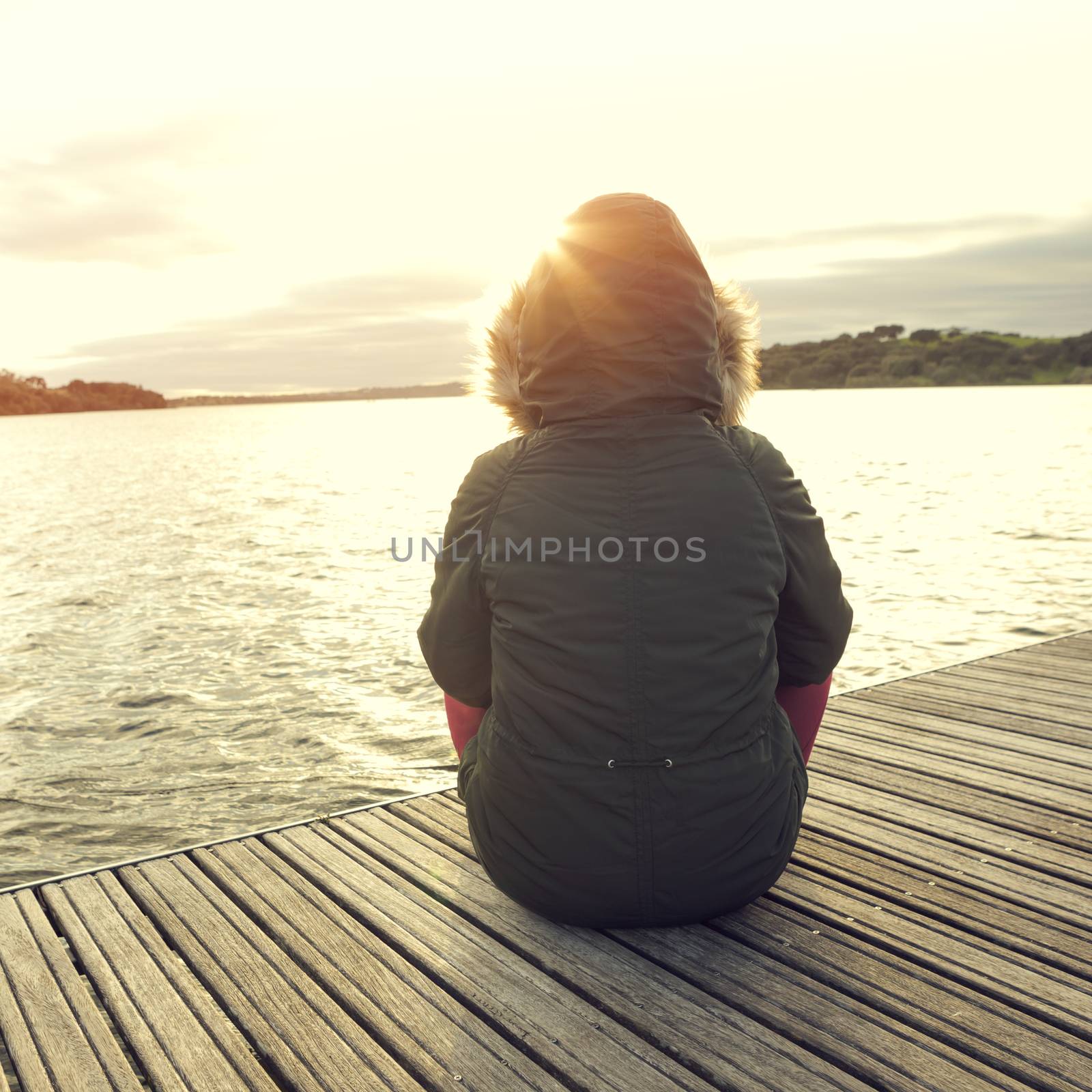 Back view of a woman sitting close to a lake