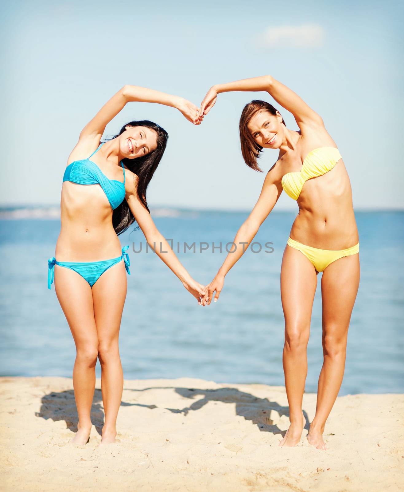 summer holidays and vacation - girls in bikinis making heart shape with hands on the beach