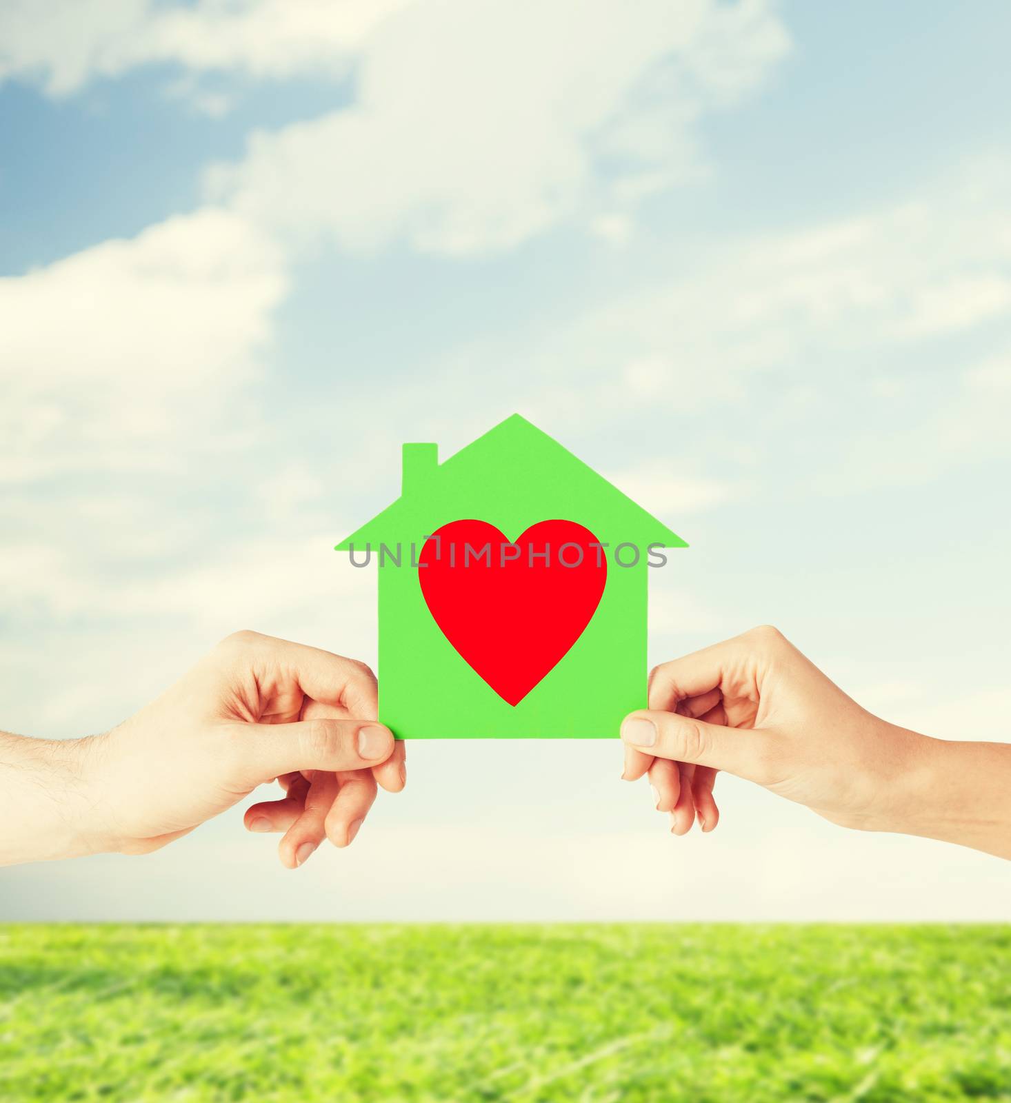 charity, real estate and family home concept - isolated picture of male and female hands holding green paper house with red heart