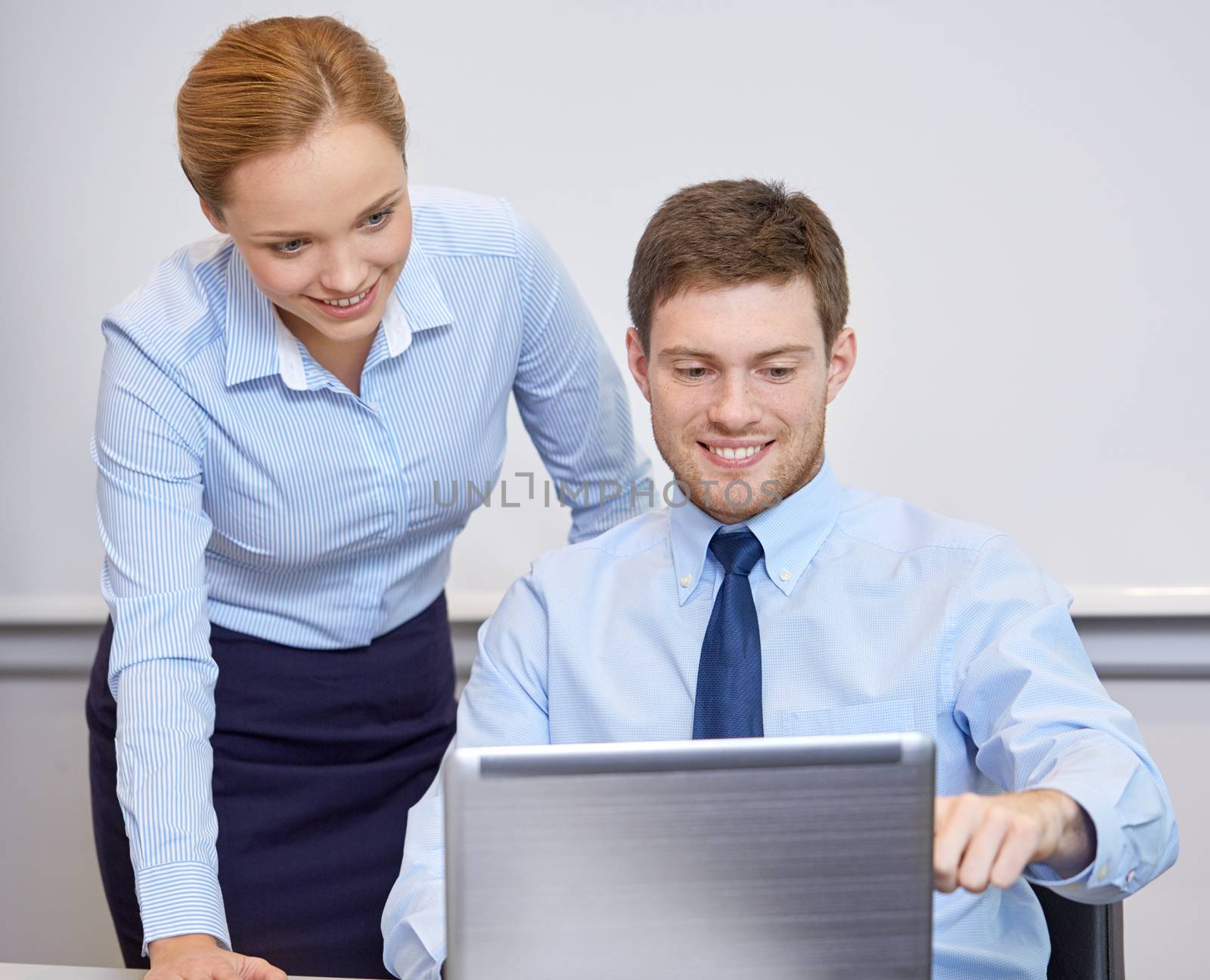 smiling businesspeople with laptop in office by dolgachov