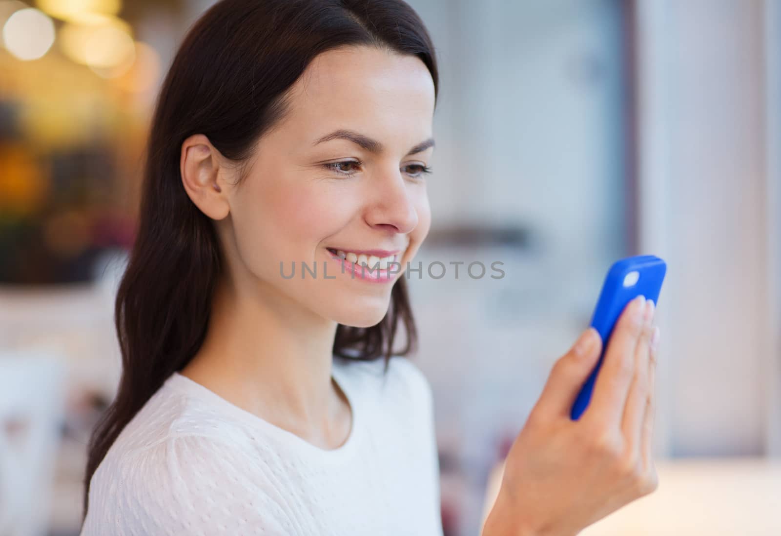 people, technology and lifestyle concept - close up of smiling young woman reading message from smartphone at cafe