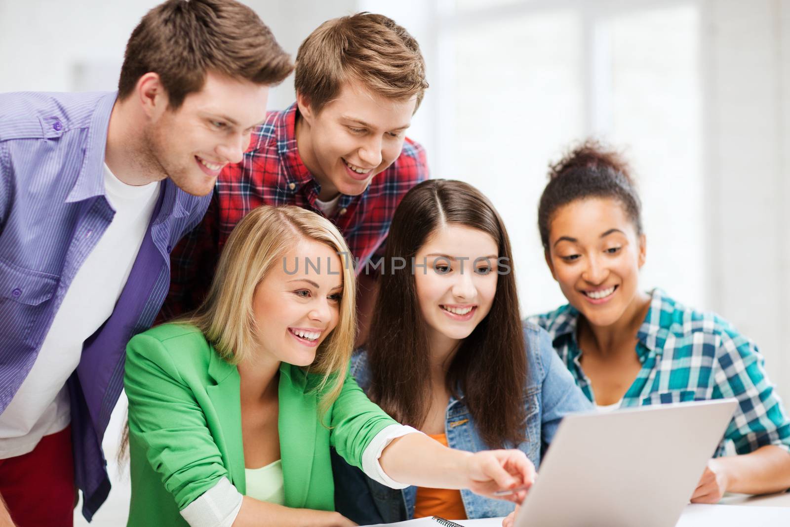 smiling students looking at laptop at school by dolgachov