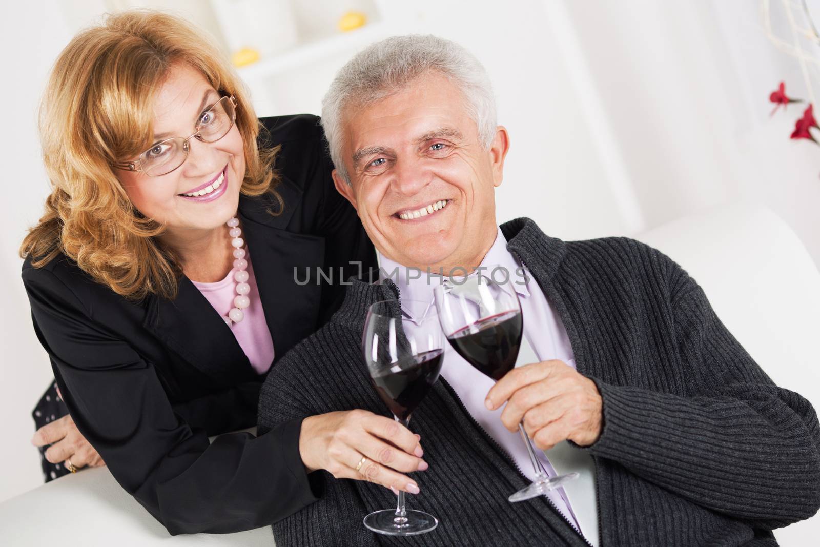 Senior couple in home interior enjoying in glass of wine.