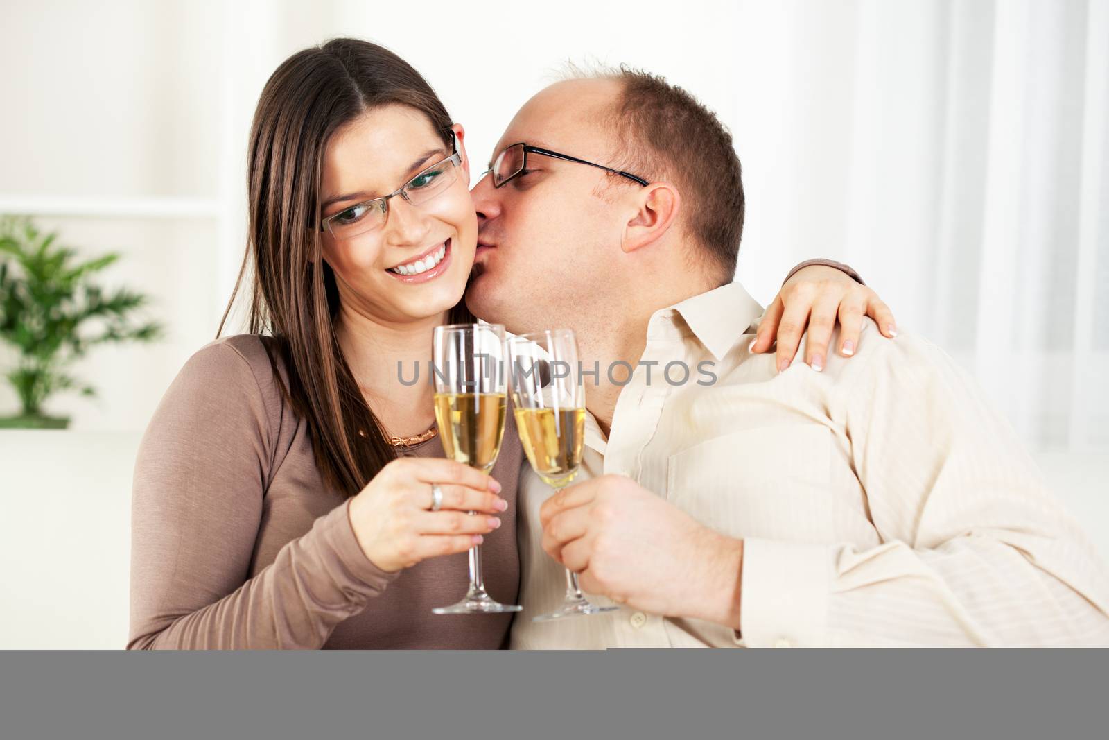 Happy Young couple in home interior enjoying in glass of champagne and kissing.