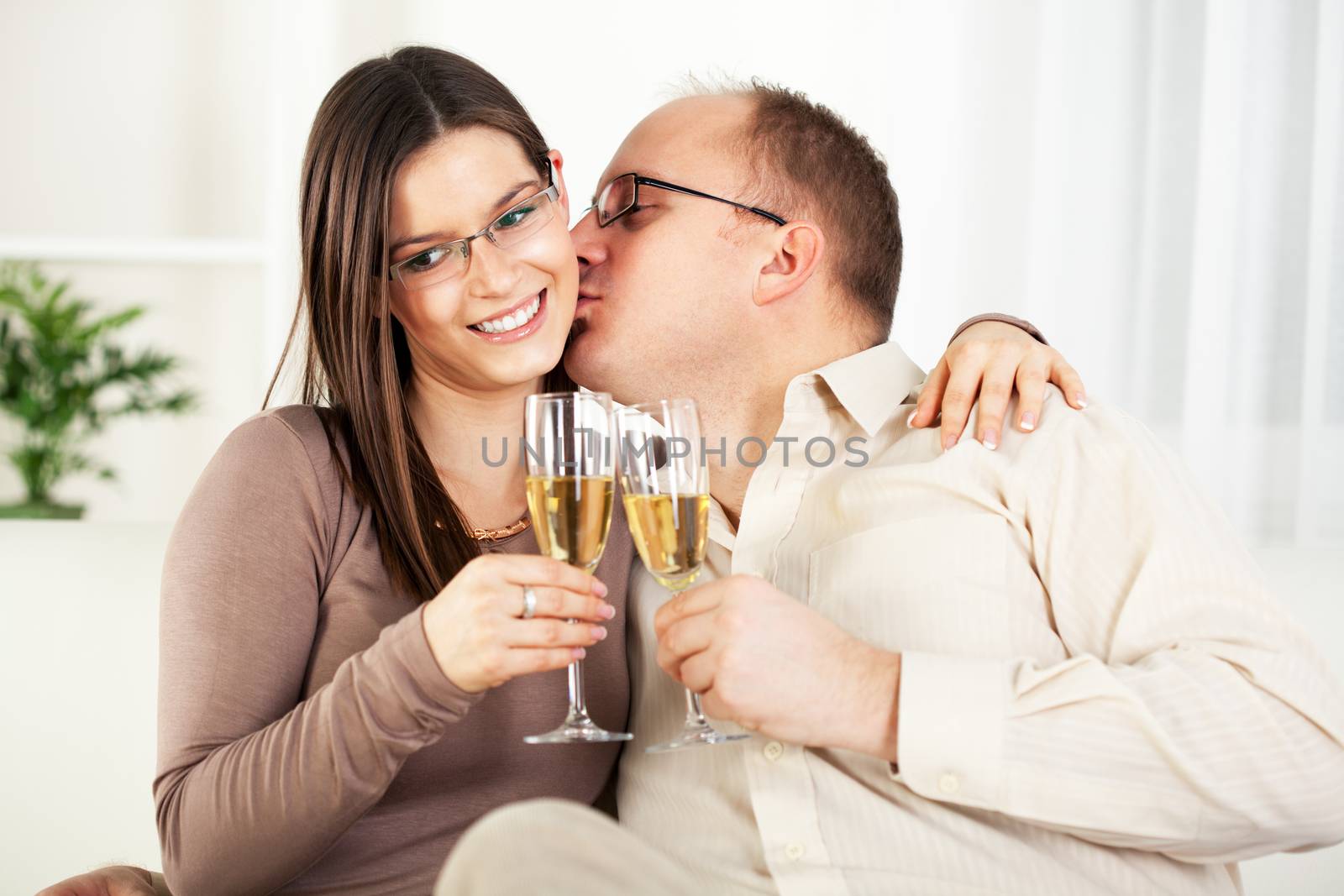 Happy Young couple in home interior enjoying in glass of champagne and kissing.