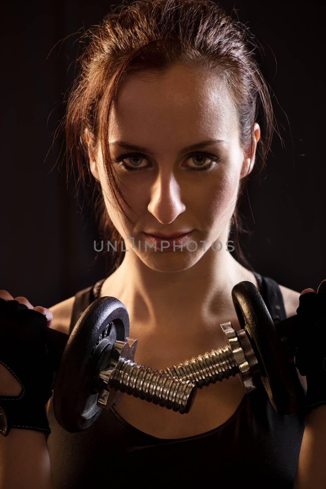 Portrait of a beautiful woman exercising with dumbbells on black background.