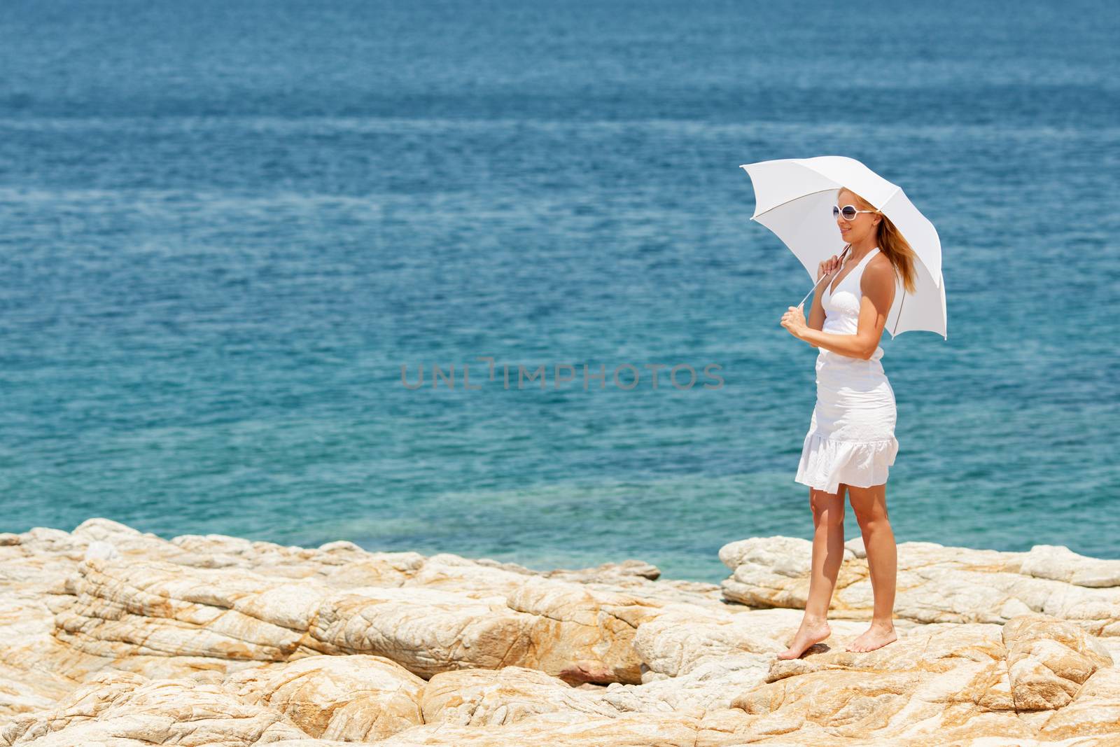 Beautiful Young Woman with white umbrella walking barefooted on stone beach.