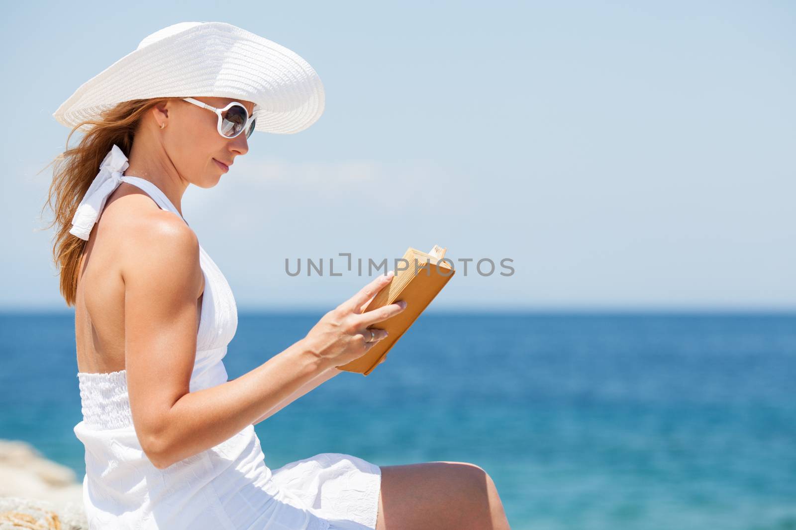 Young beautiful woman reading book and relaxing on the beach.