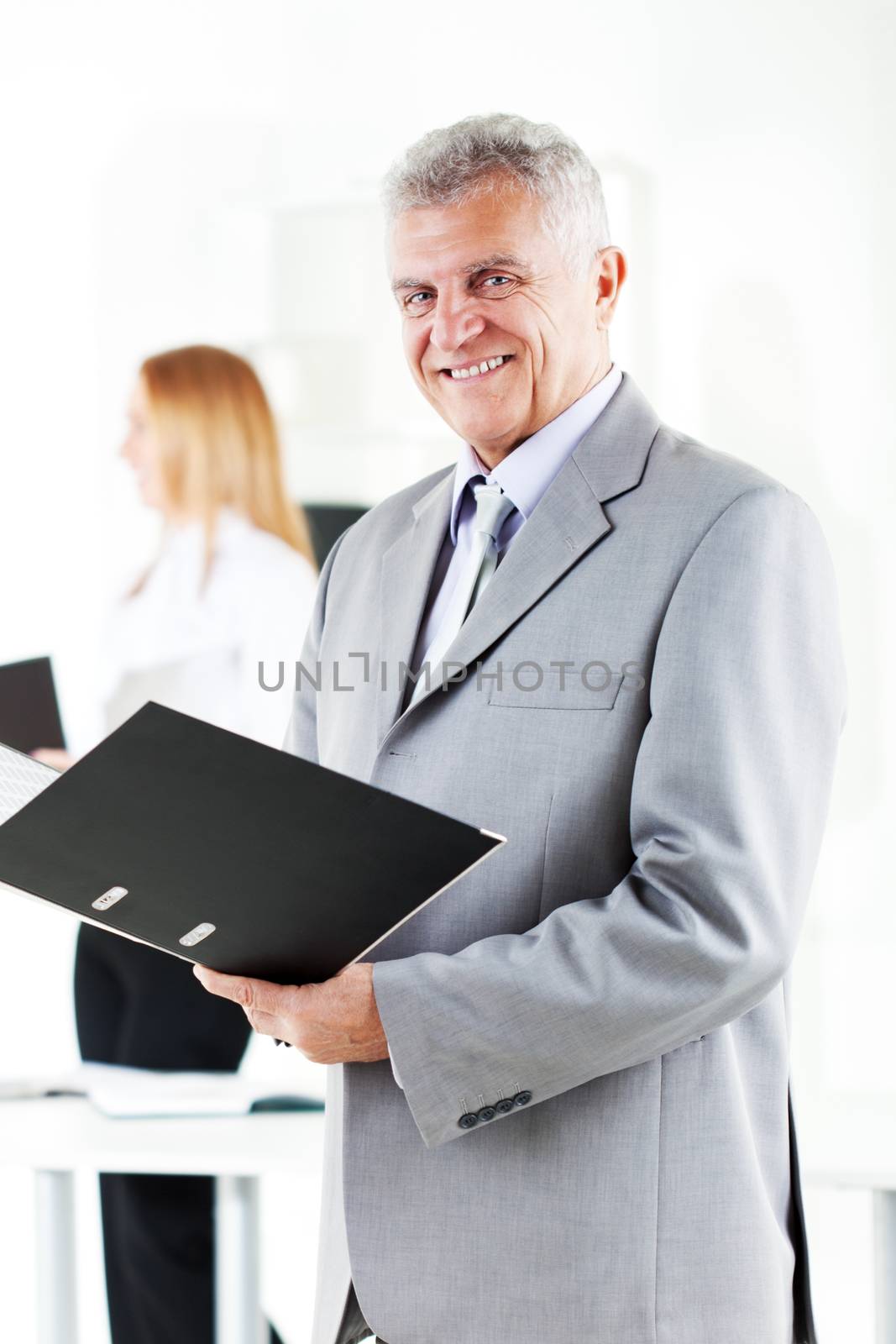 Happy senior businessman with folder standing in the office. Looking at camera. Selective Focus.