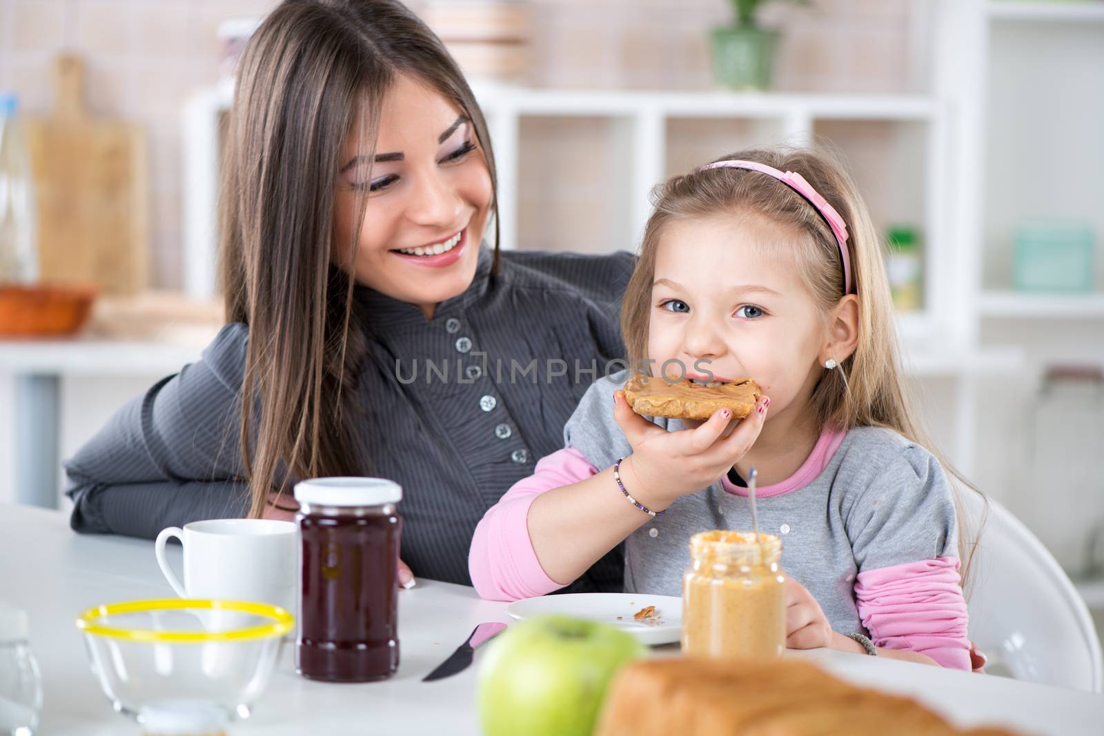 Mother and daughter breakfast in the kitchen. Cute little girl eats bread with peanut butter.