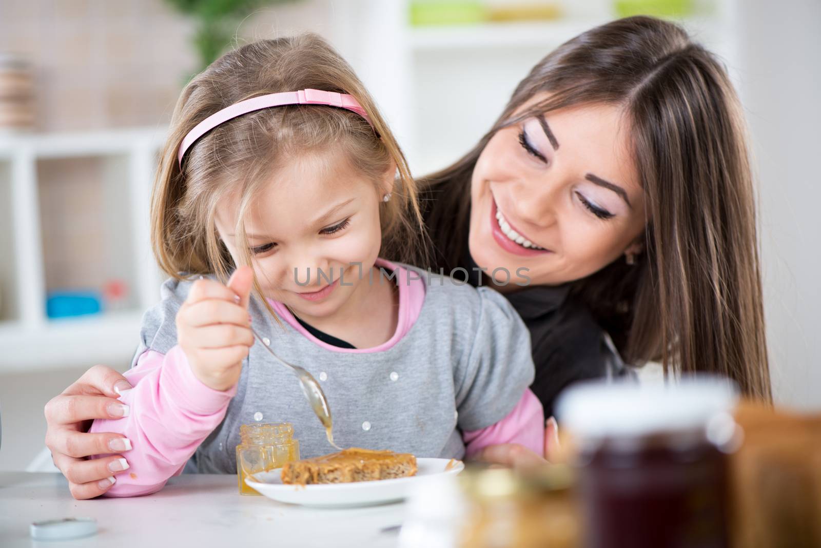 Mother and daughter preparing breakfast. They smear honey over the peanut butter on bread.