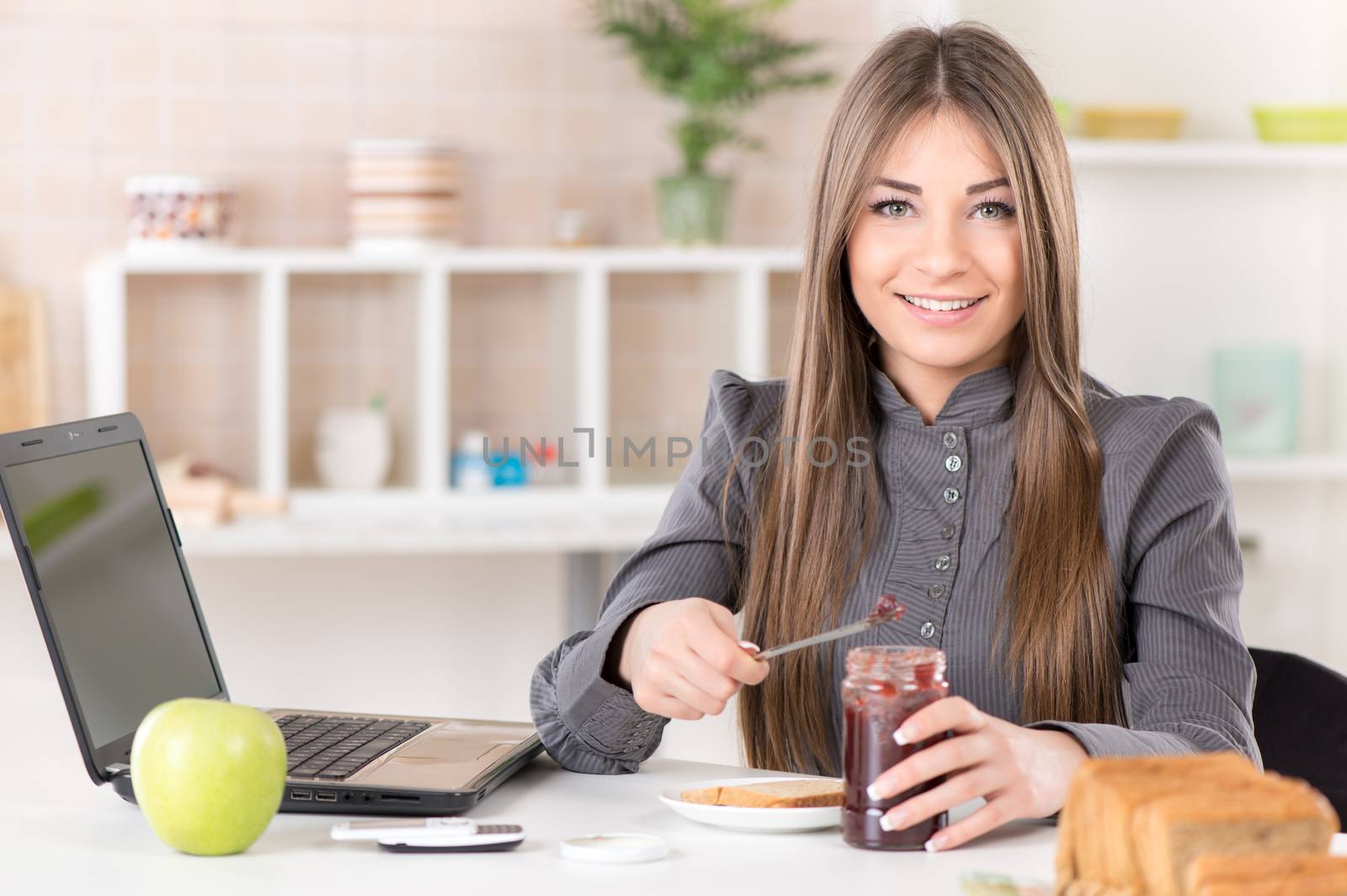 Businesswoman in the kitchen preparing breakfast. She is smearing jam on bread before going to work.