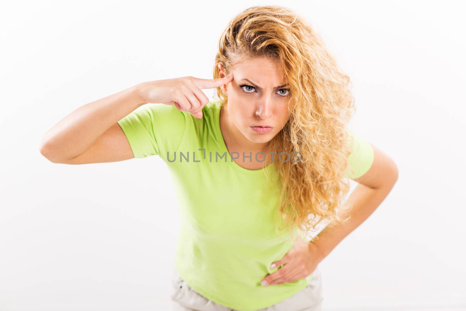Angry young woman standing against a white background with a finger pressed against the head.