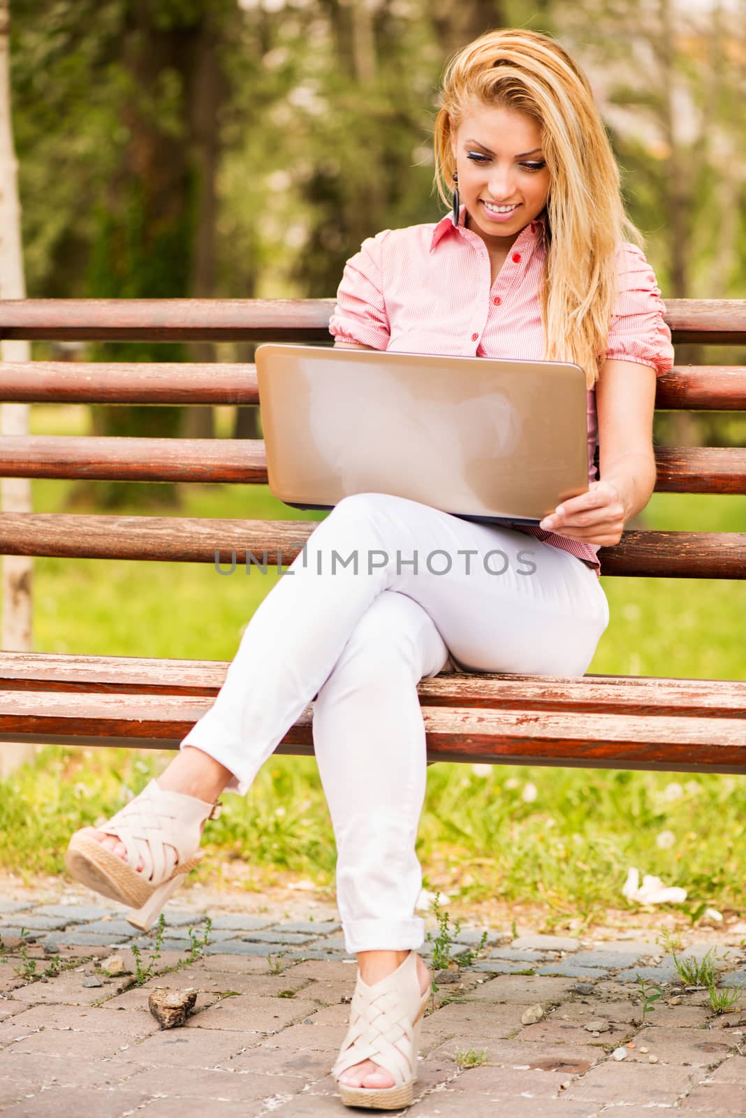 Young Beautiful Woman sitting and relaxing on the Park Bench and using laptop.