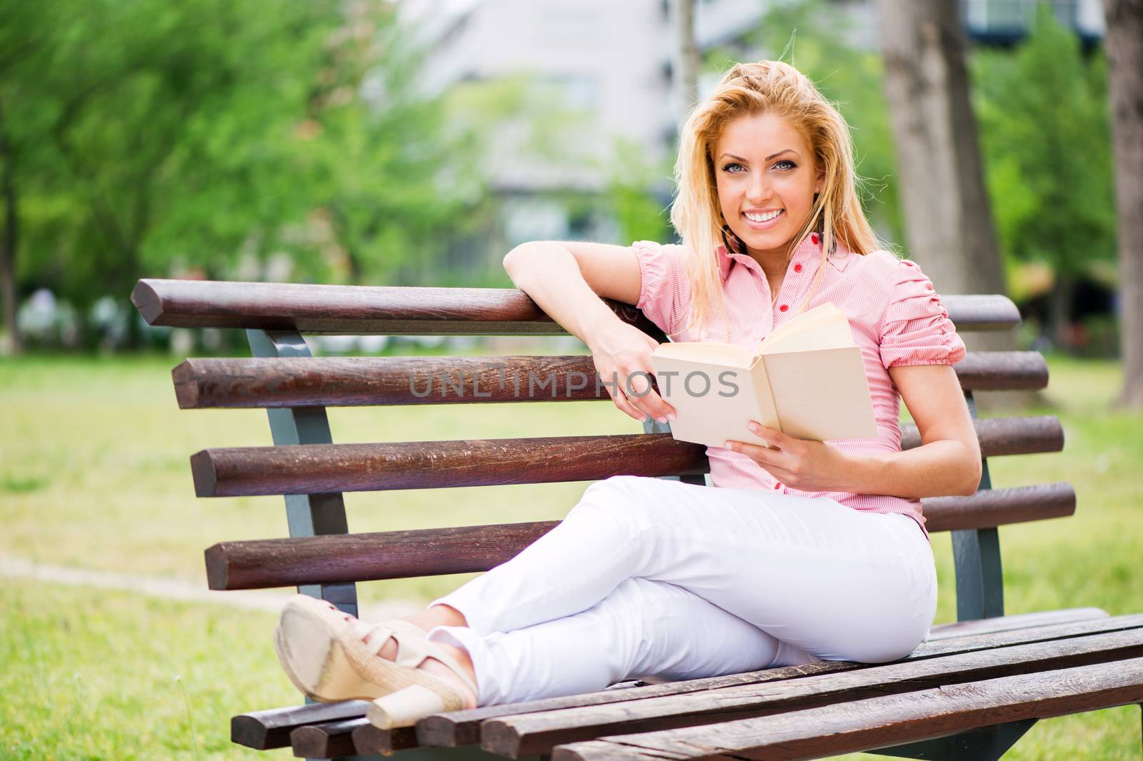 Young Beautiful Woman Reading Book In The Park, and sitting on the Park Bench.