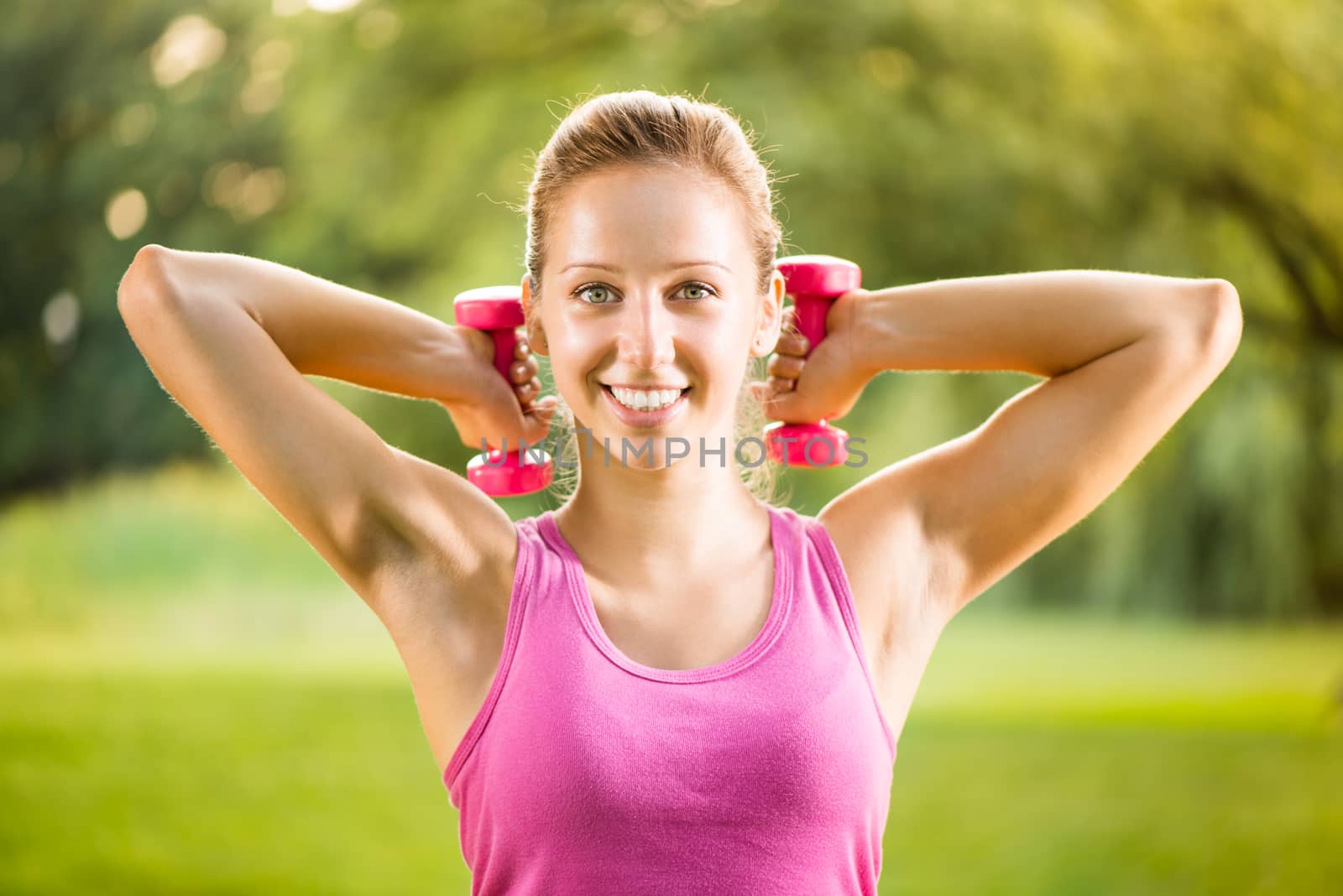 Portrait of Beautiful young woman exercising with weights in the park.