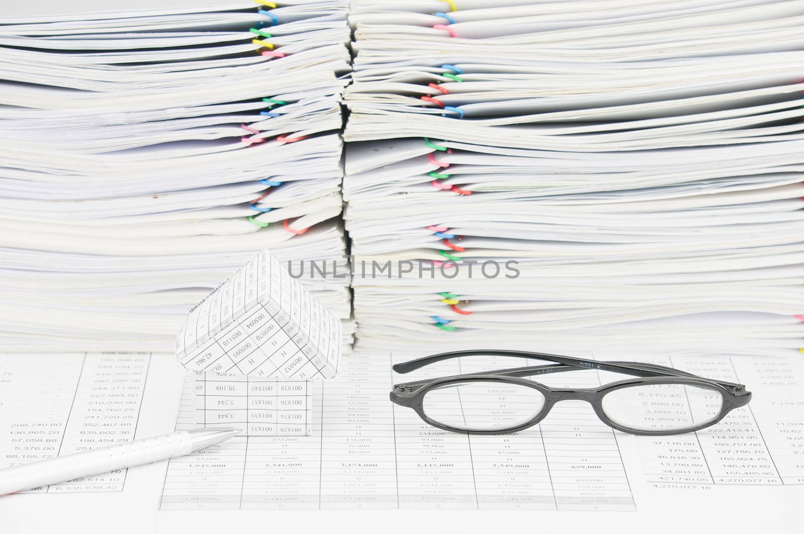 Silver pen and house with spectacles on finance account have paperwork and paper of report as background.