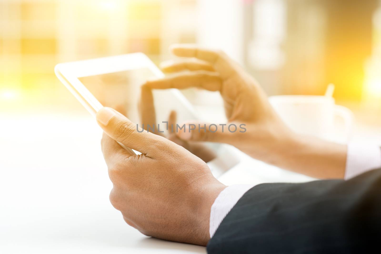 Close-up of Indian male hands touching digital tablet, formal businessman with cup of coffee on table, focus on hand with bokeh and light.