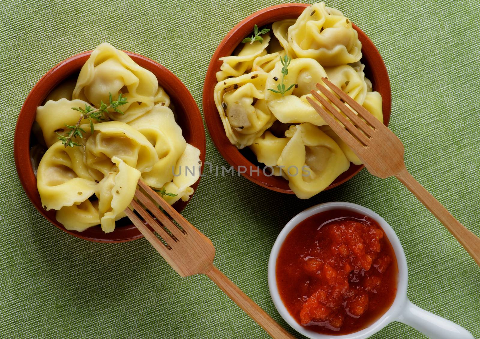 Delicious Meat Cappelletti in with Tomatoes Sauce and Wooden Forks closeup on Green Napkin background. Top View