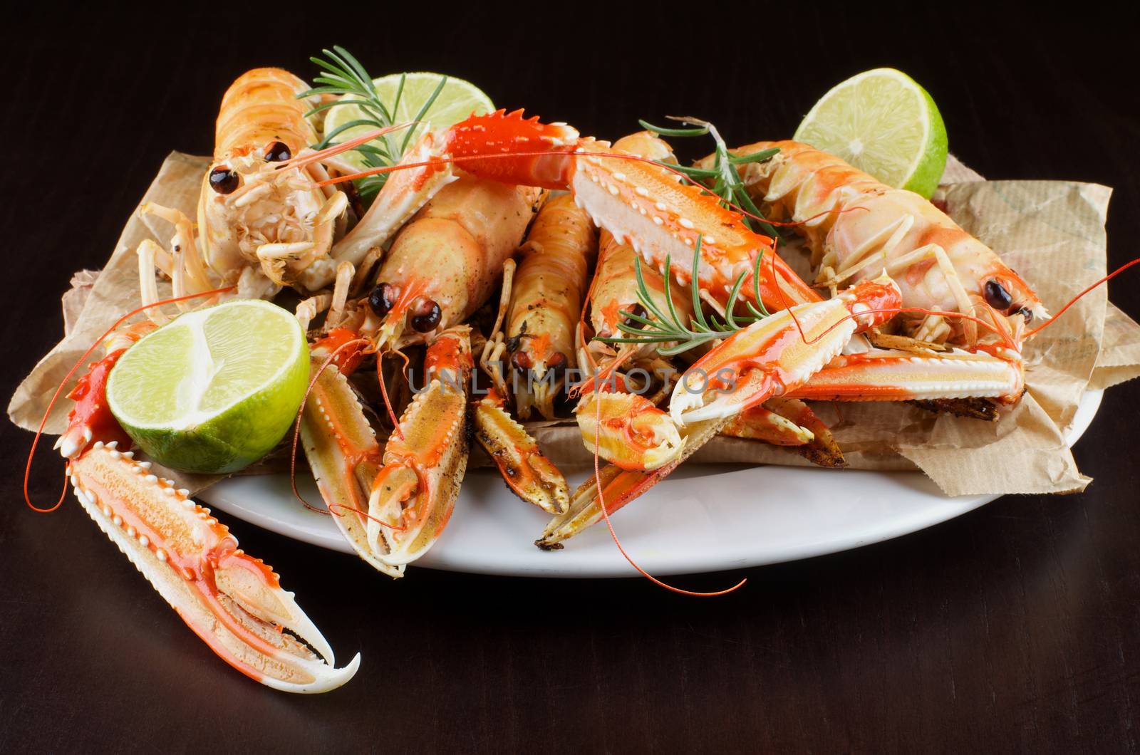 Delicious Grilled Langoustines with Lime and Rosemary on White Plate closeup on Dark Wooden background