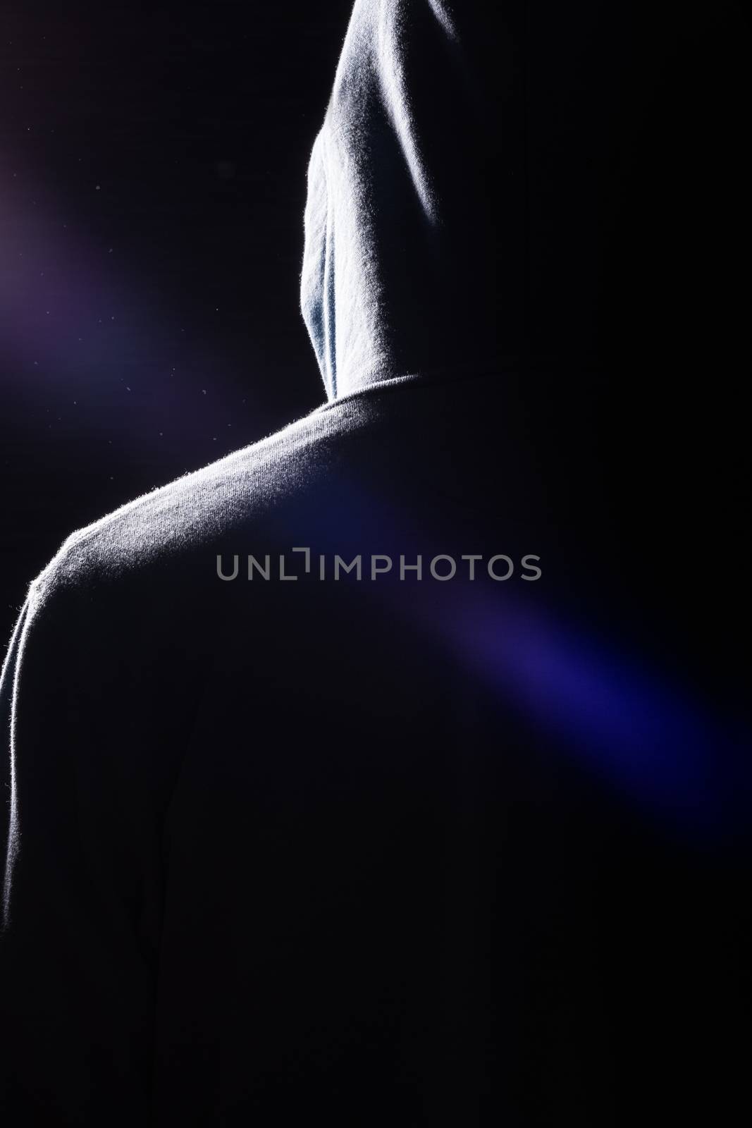 A dark silhouette of a man wearing a hooded sweatshirt with very dramatic shadows, lens flare and dust in the air.