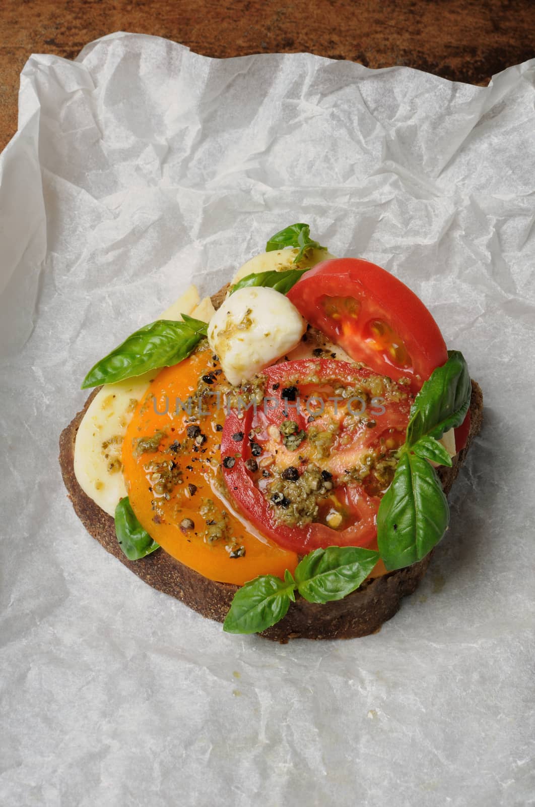 sandwich of rye bread mozzarella, tomato and pesto wrapped in baking paper