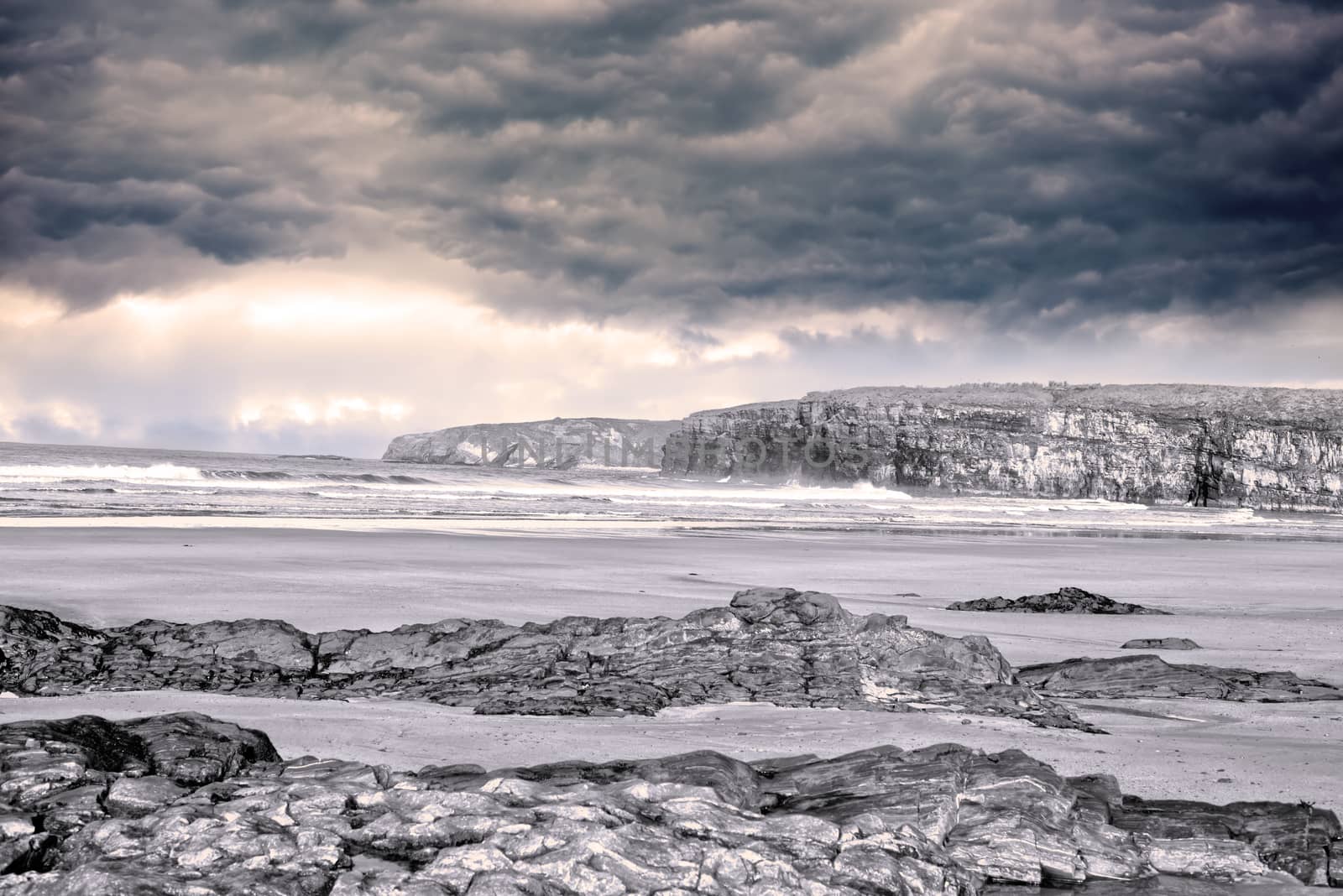 storm clouds with soft waves break on the beach and rocky sand at ballybunion