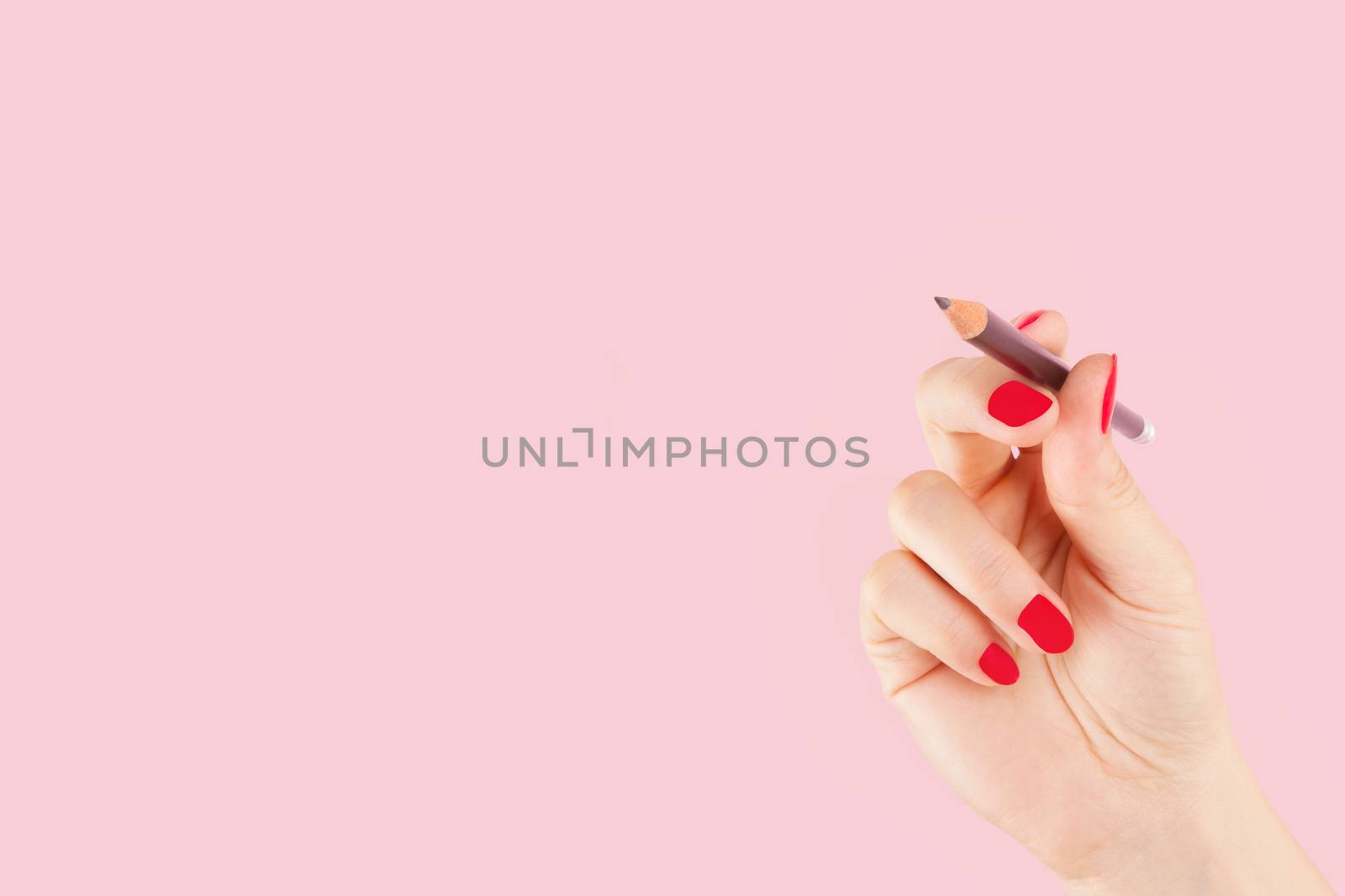 Female hand with red fingernails holding a pencil isolated on pink background. Creativity and copy writing, teaching and learning. 