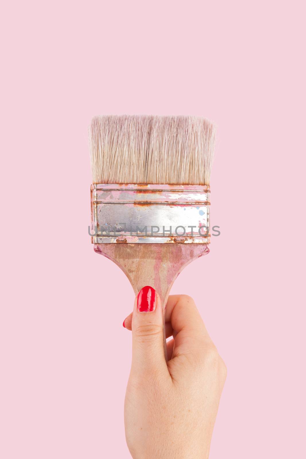 Female hand with red fingernails holding paintbrush isolated on pink background. Creative painting. 