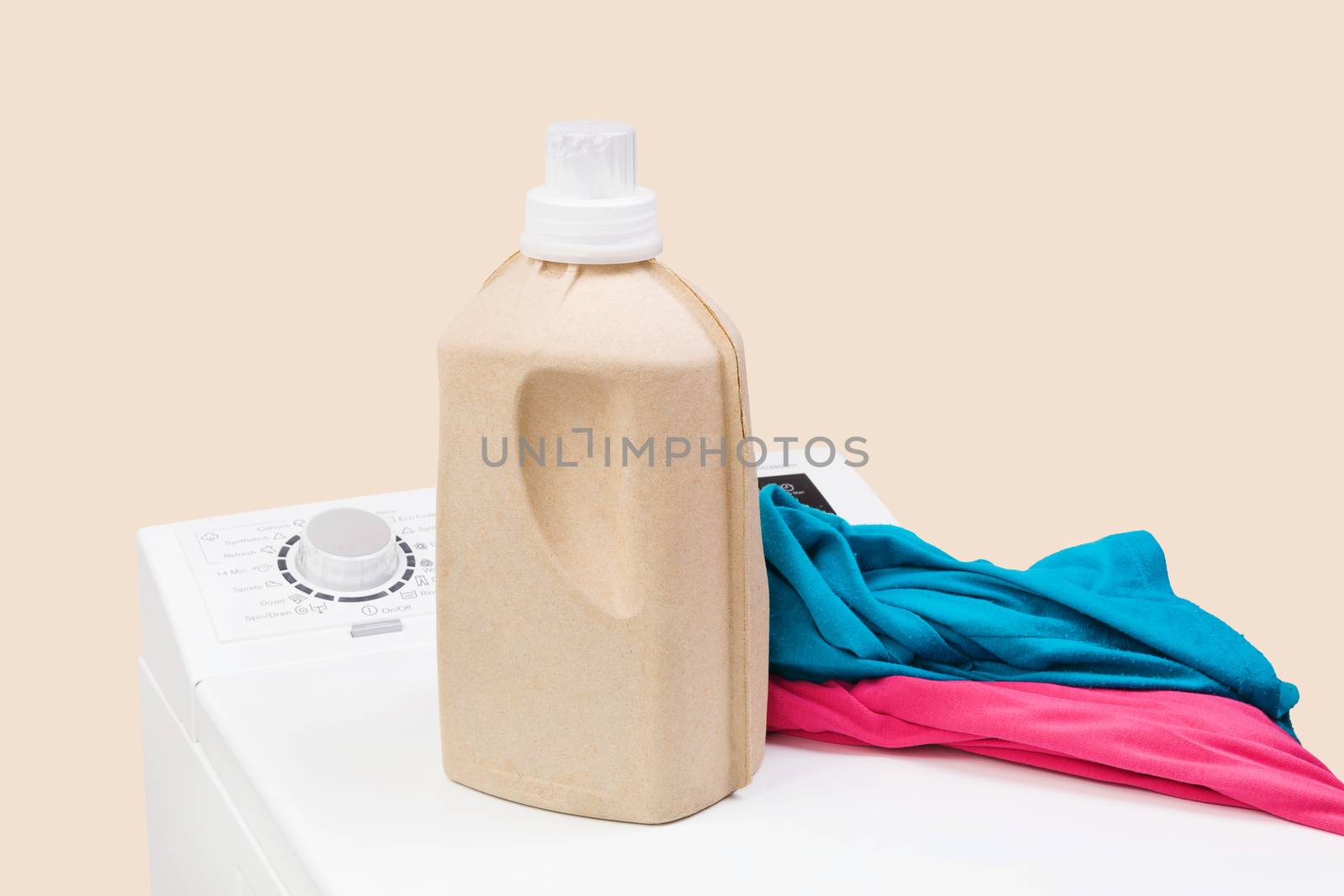 Laundry background. Top loading washing machine with natural organic detergent and colorful clothing isolated on beige background. 