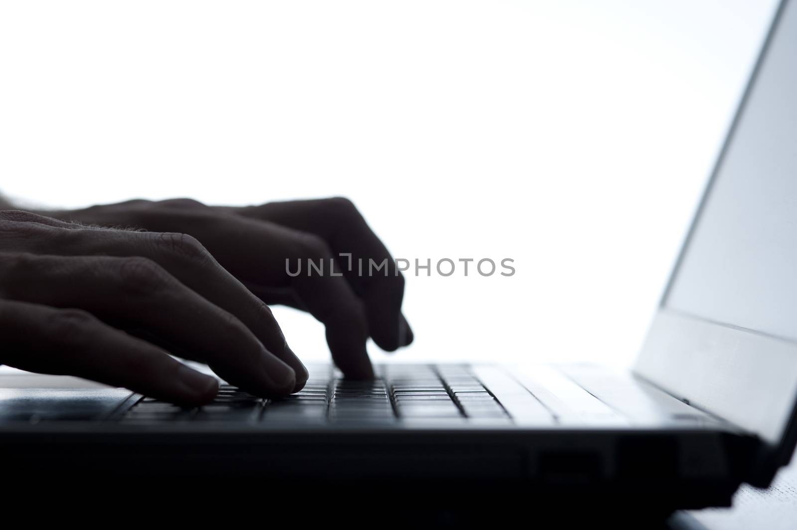 Low angle silhouette of the hands of a person typing on a laptop keyboard isolated on white with copyspace