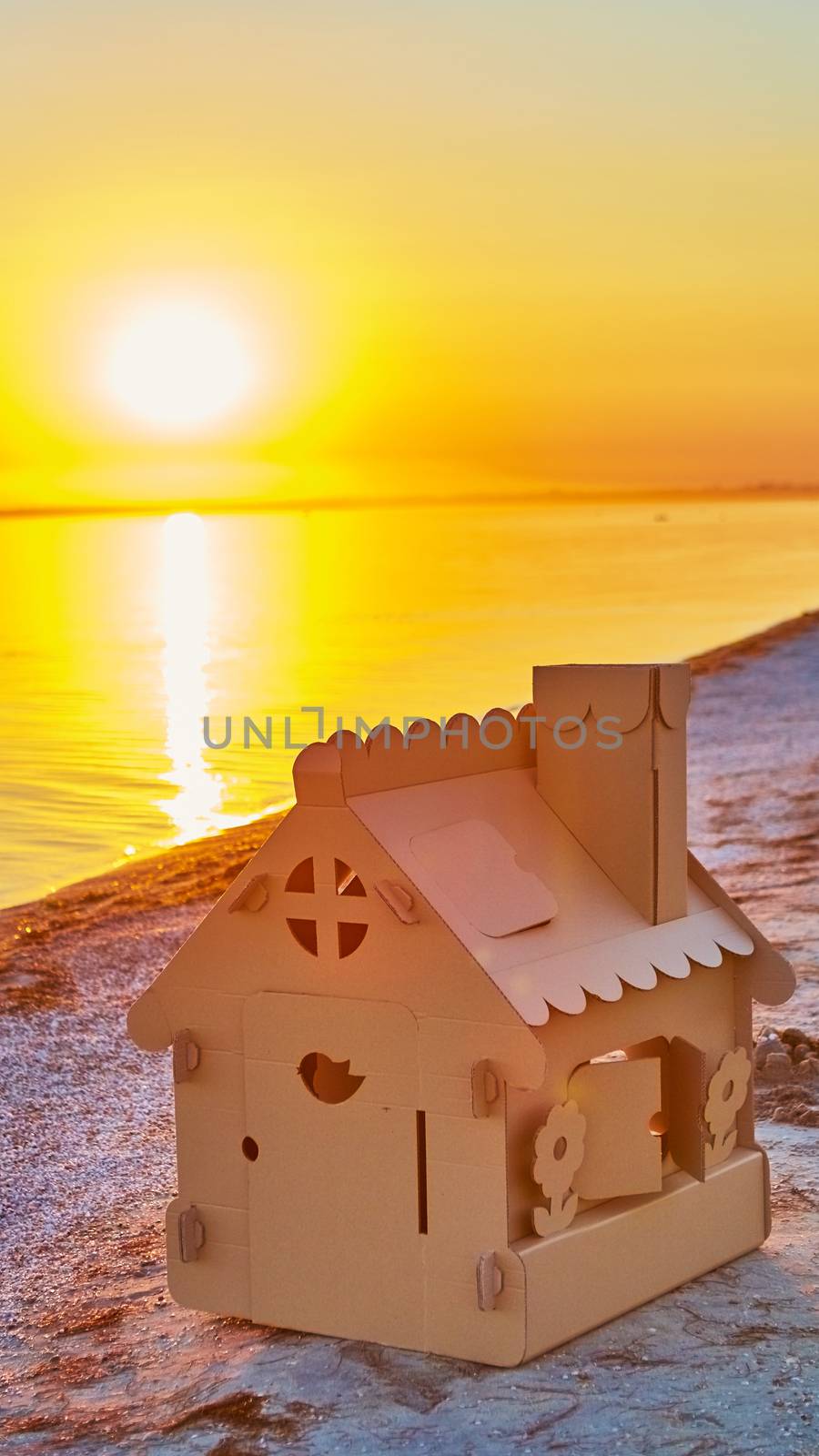 Toy house made of corrugated cardboard in the sea coast at sunset. by sarymsakov