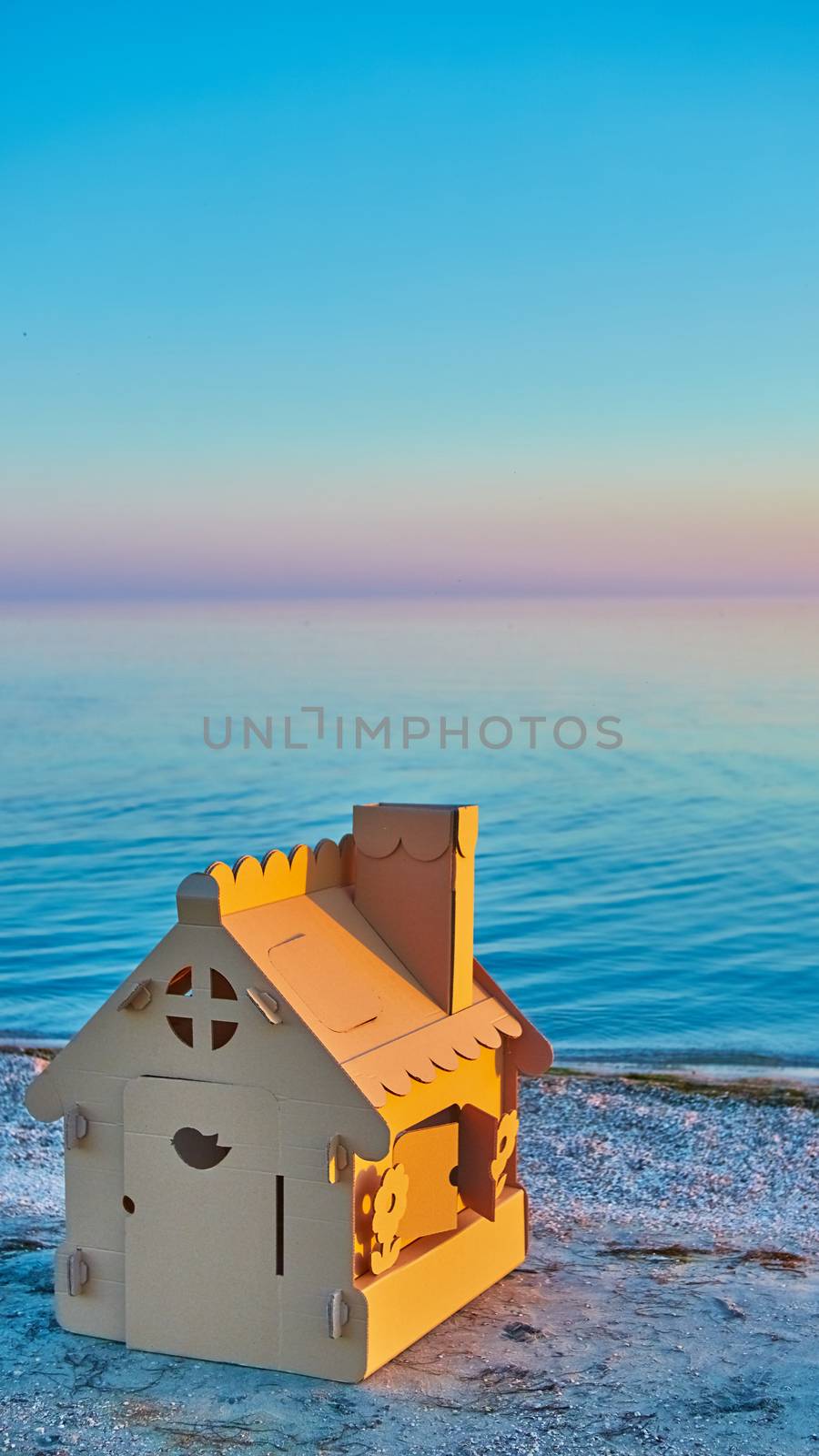 Toy house made of corrugated cardboard in the sea coast at sunset. The concept of eco-estate