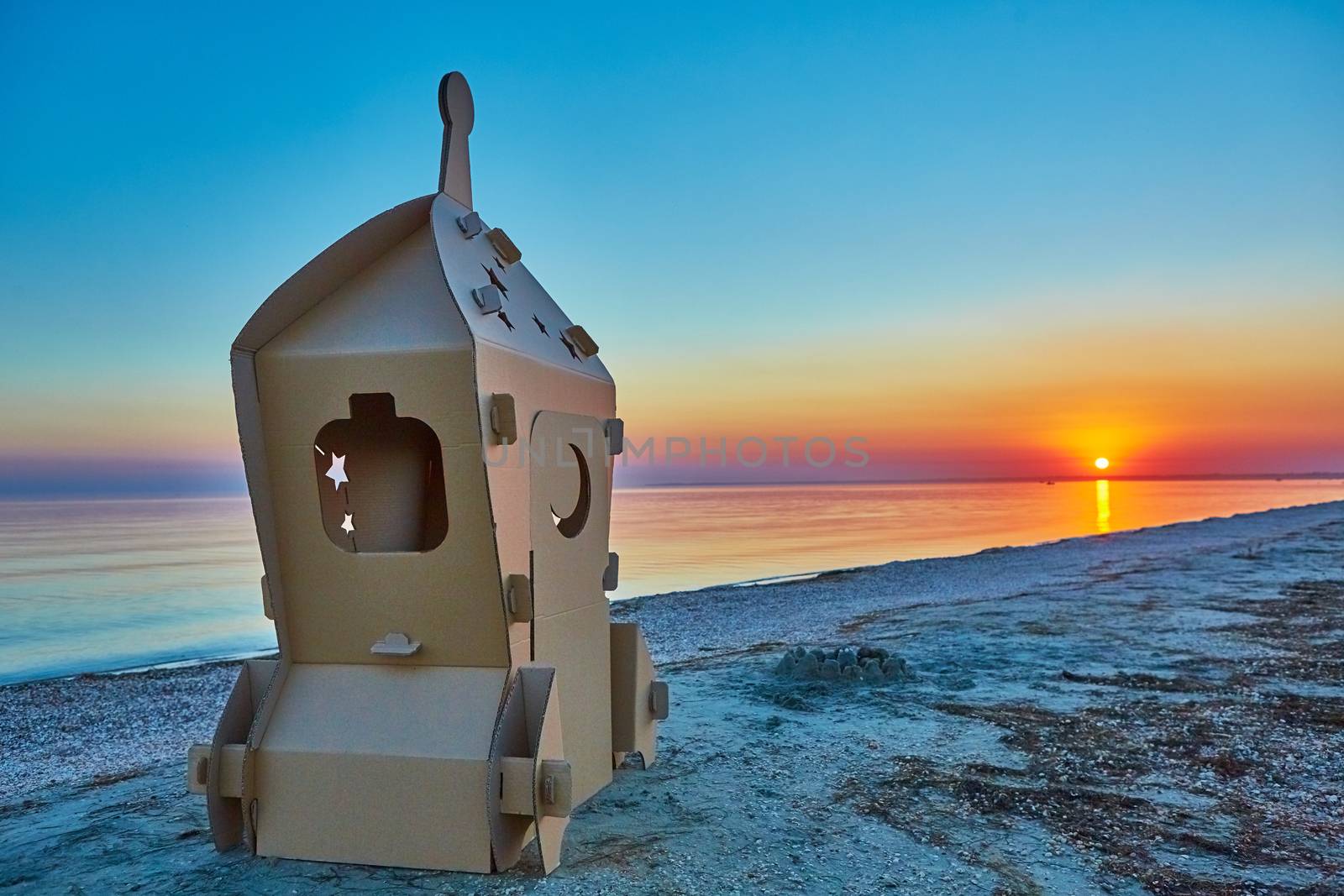Cardboard toy spaceship at sea coast and sunset. Eco concept