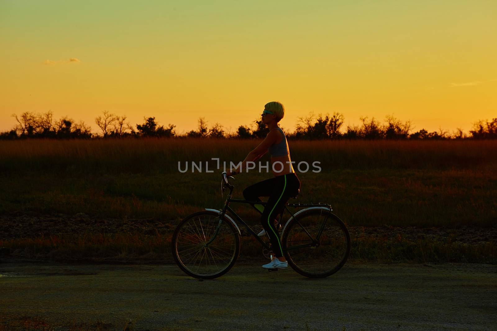 Biker girl at the sunset on the meadow