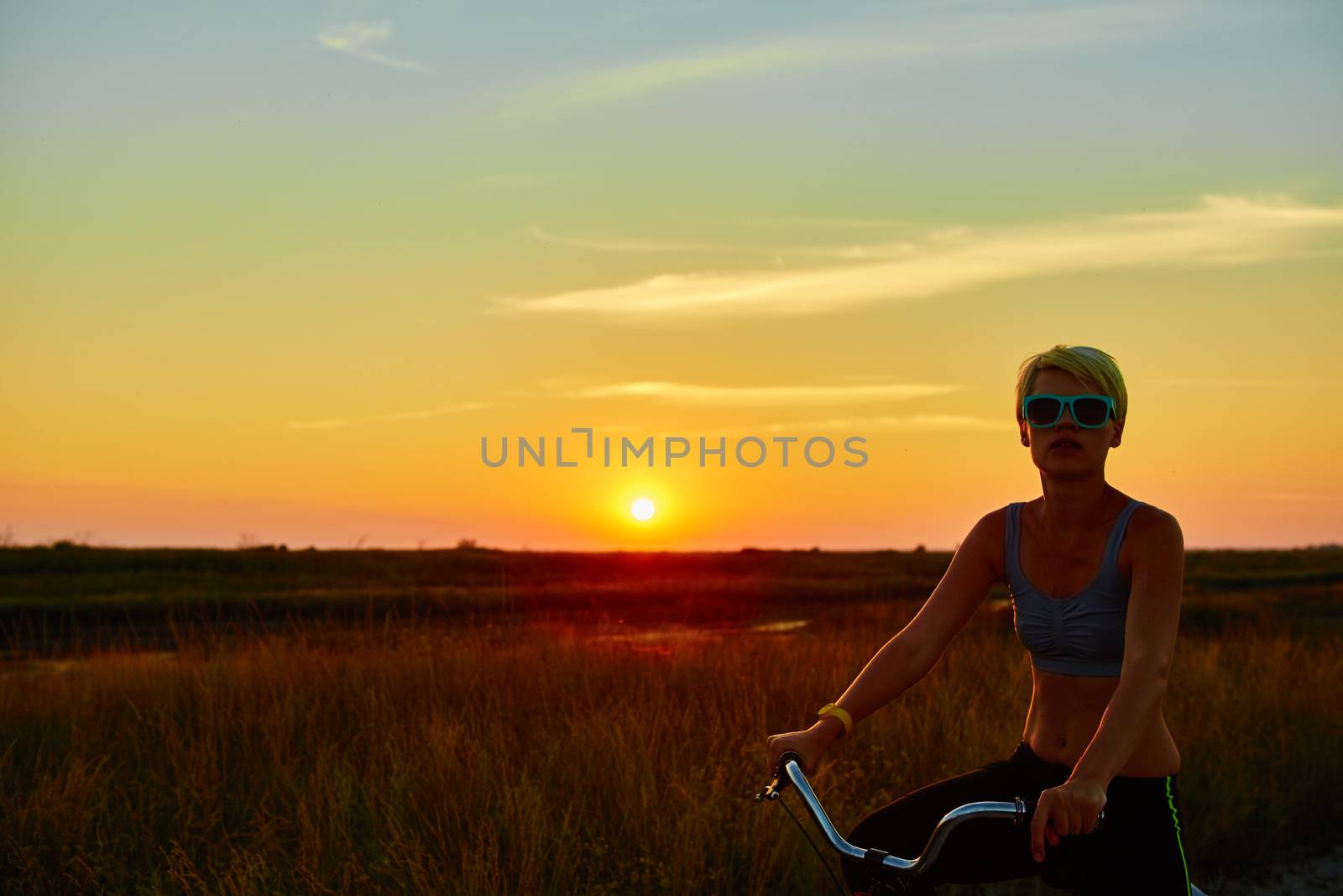 Biker girl at the sunset on the meadow