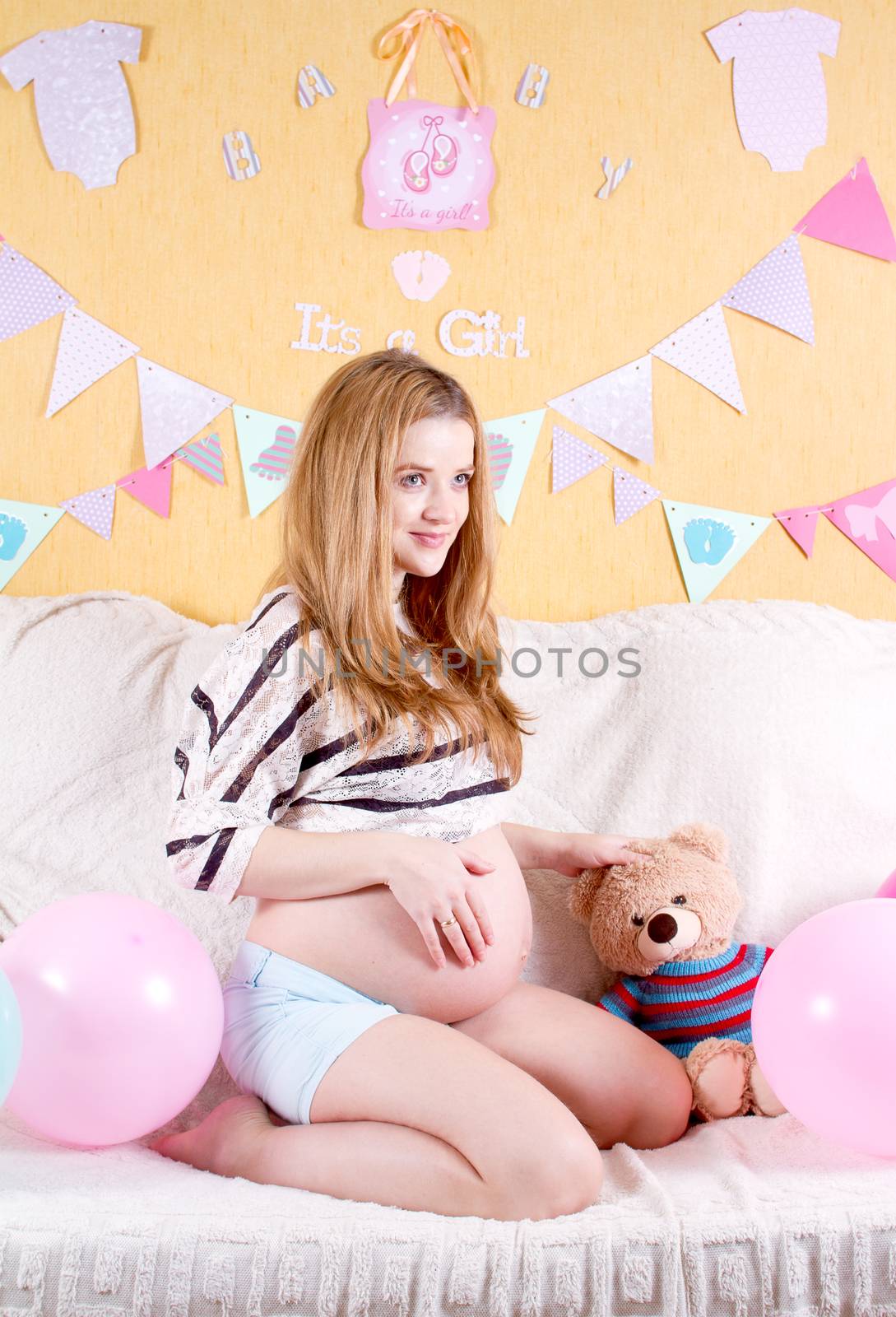 Pregnant smiling woman sitting on a sofa and caressing her belly.